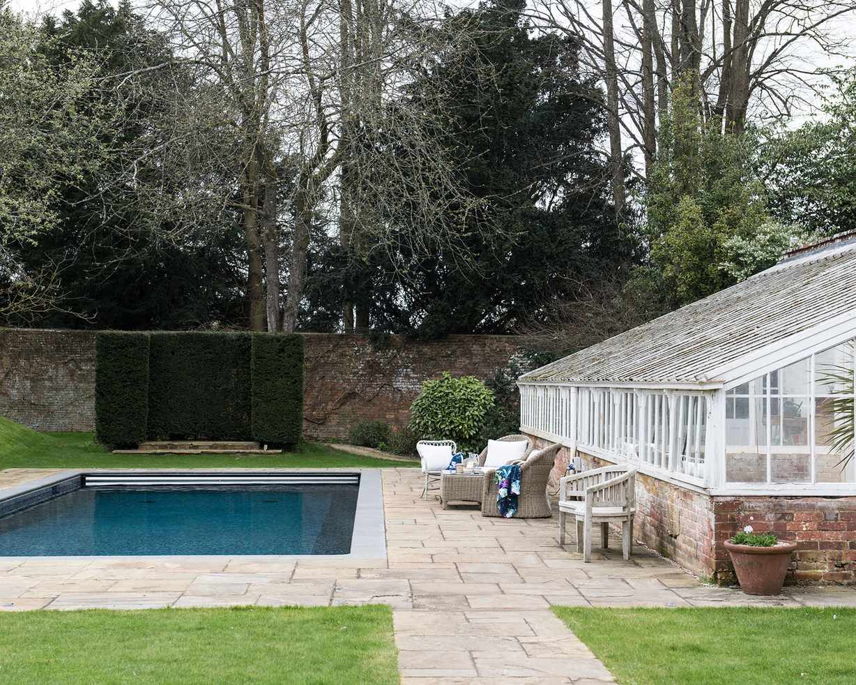 An example of pool landscaping ideas showing a traditional garden room with glass panels, pavers and a small pool