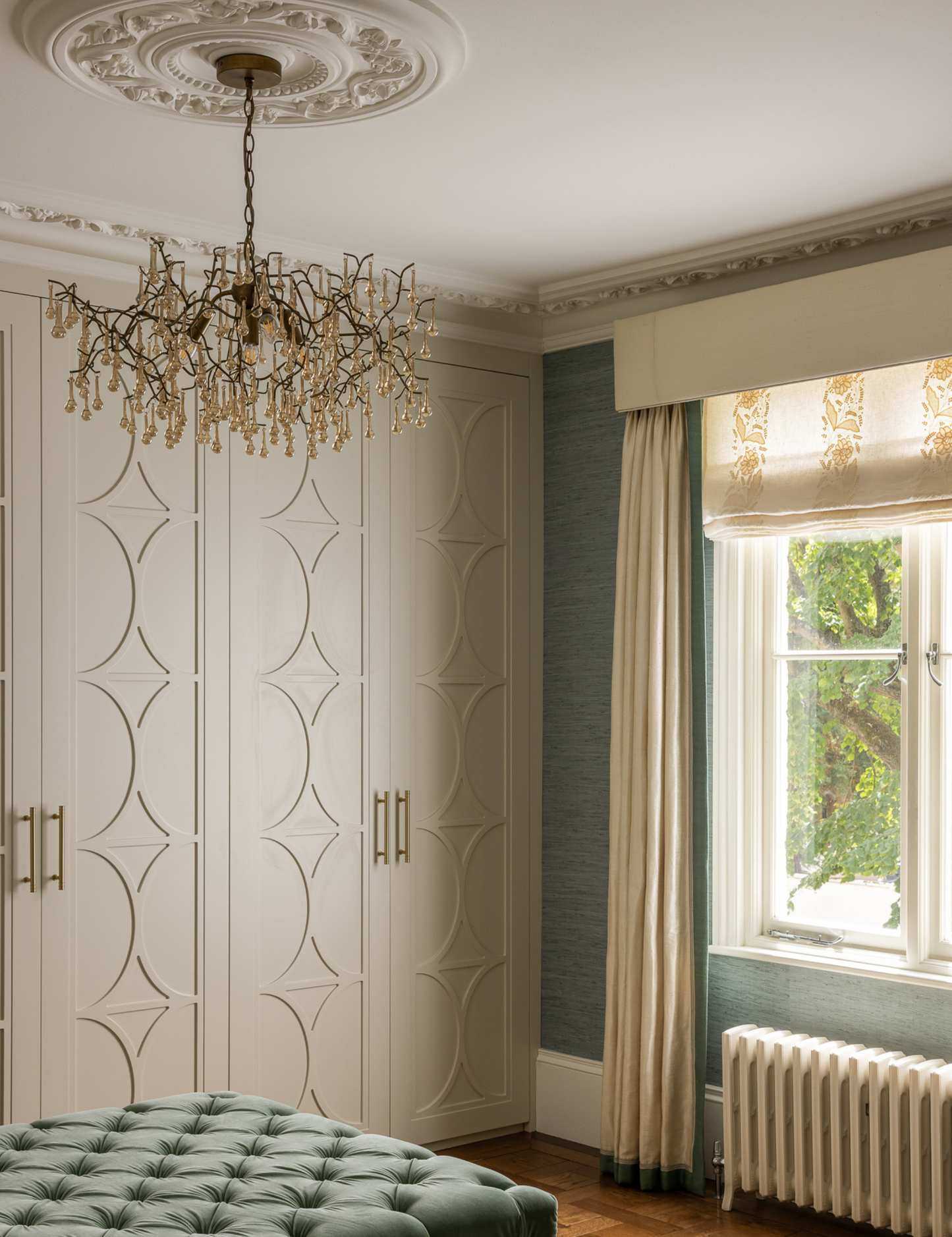 Ornate dressing room featuring a crystal chandelier, sky blue tufted ottoman, and layered window treatments