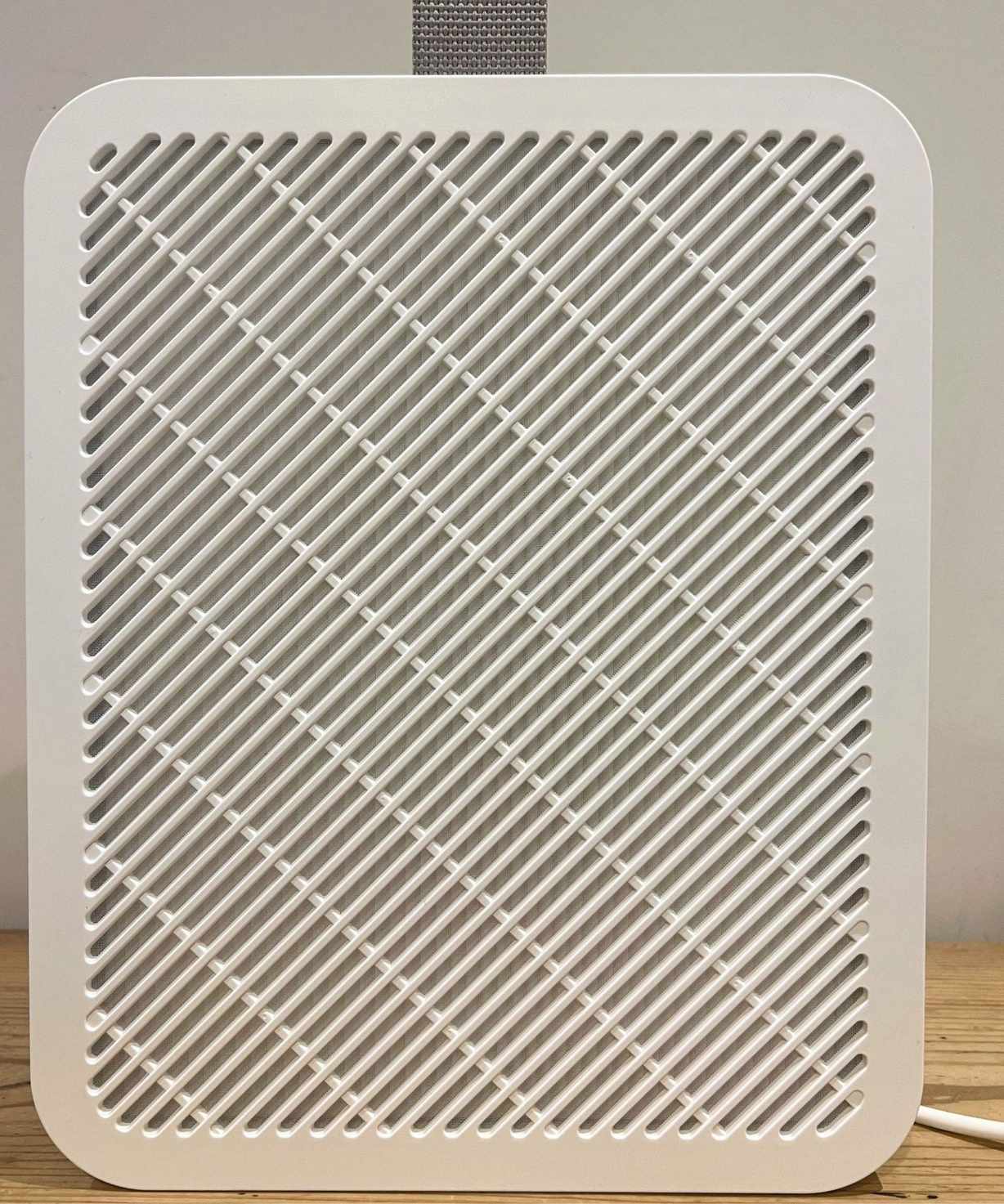 A white IKEA UPPÅTVIND Air purifier with a white cable and grey carry handle on a wooden table against a white wall.