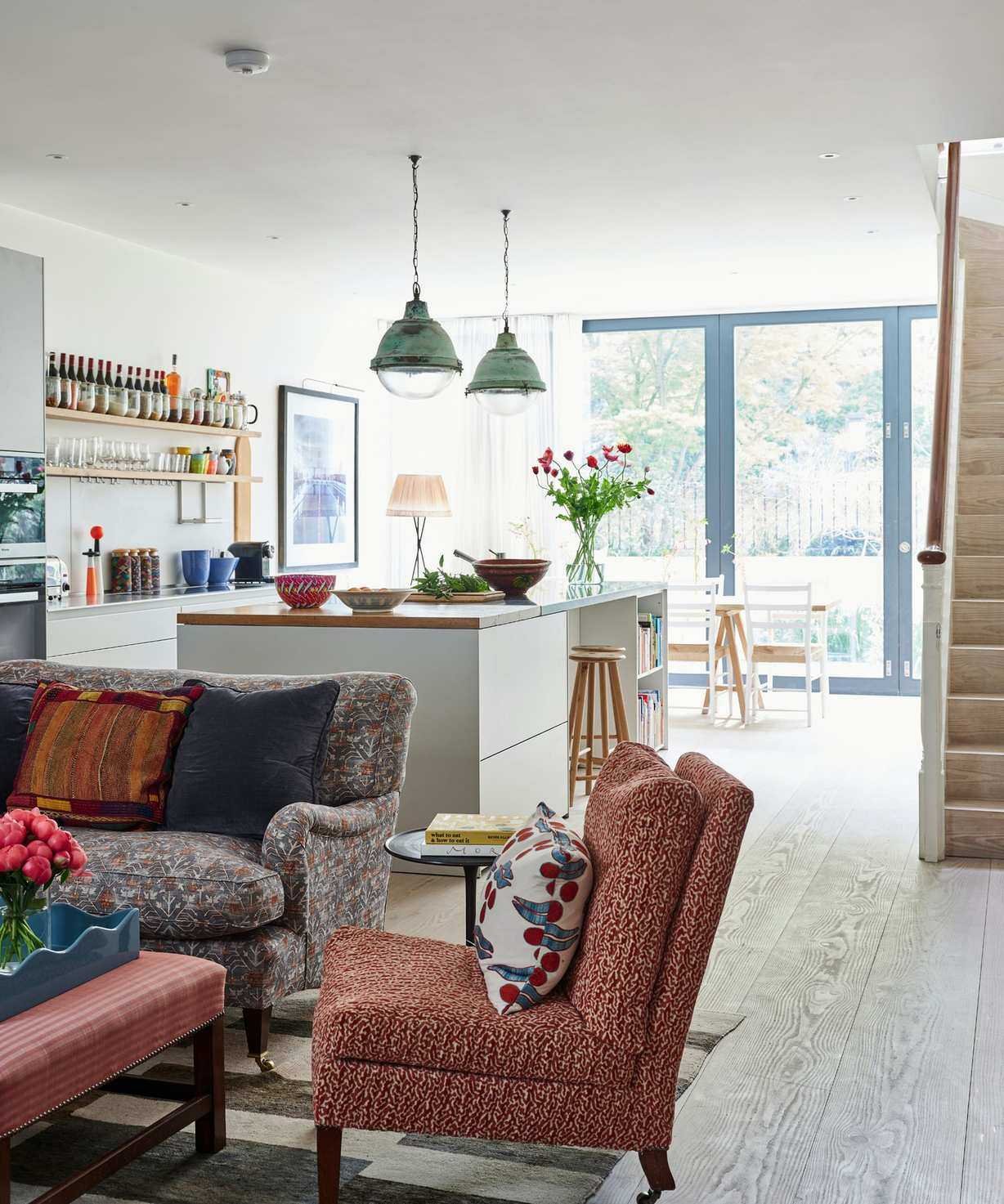 an open plan living room and kitchen with traditional furniture, a large kitchen island with pendants hanging from the ceiling, and a wall of glass doors in the background
