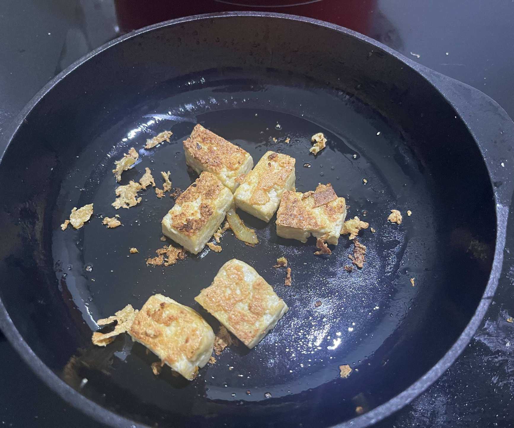 Tofu frying in a a small black cast iron skillet.