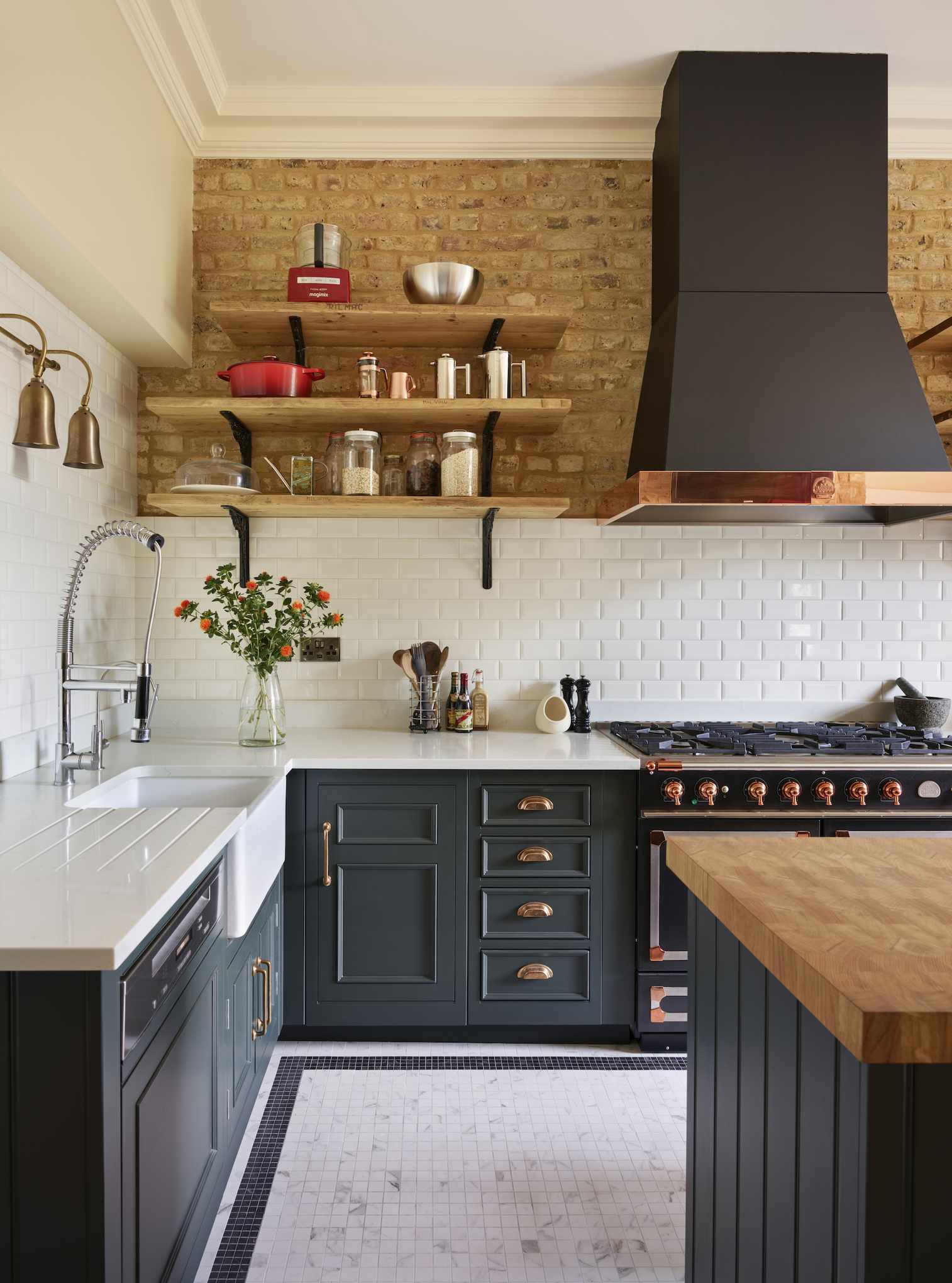 A dark blue painted kitchen, whit white subway tile backsplash, and exposed brick on the upper walls. White counters.