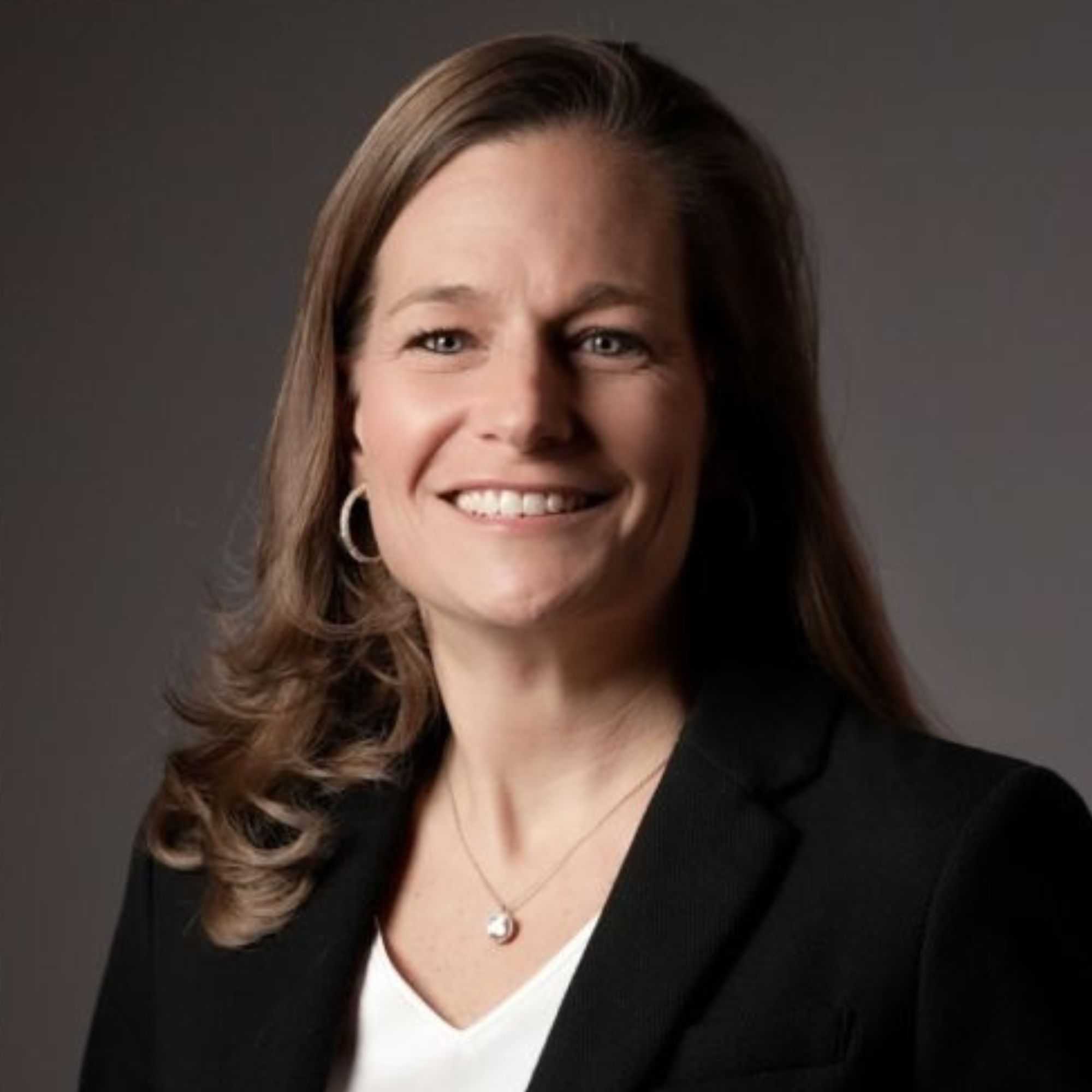 A picture of Marla Mock - a woman with brown hair wearing a black blazer and white top, smiling into the camera