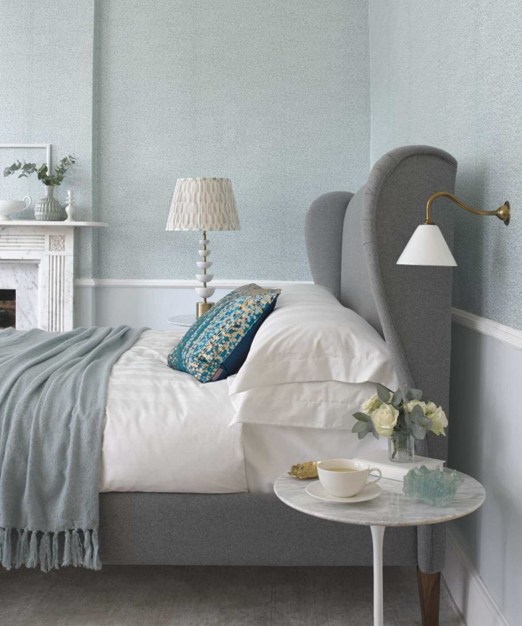 Neutral bedroom with grey bed and white bedding, white sconce and marble bedside table