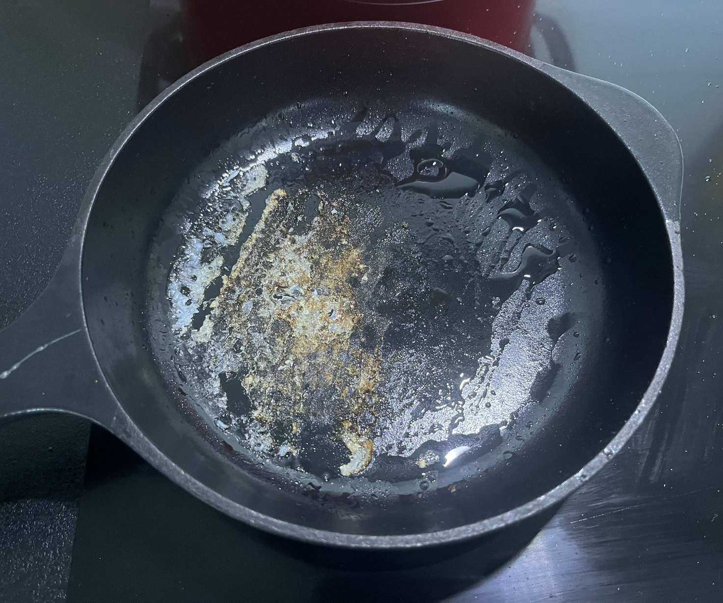A back cast iron skillet with stuck on egg in the base.
