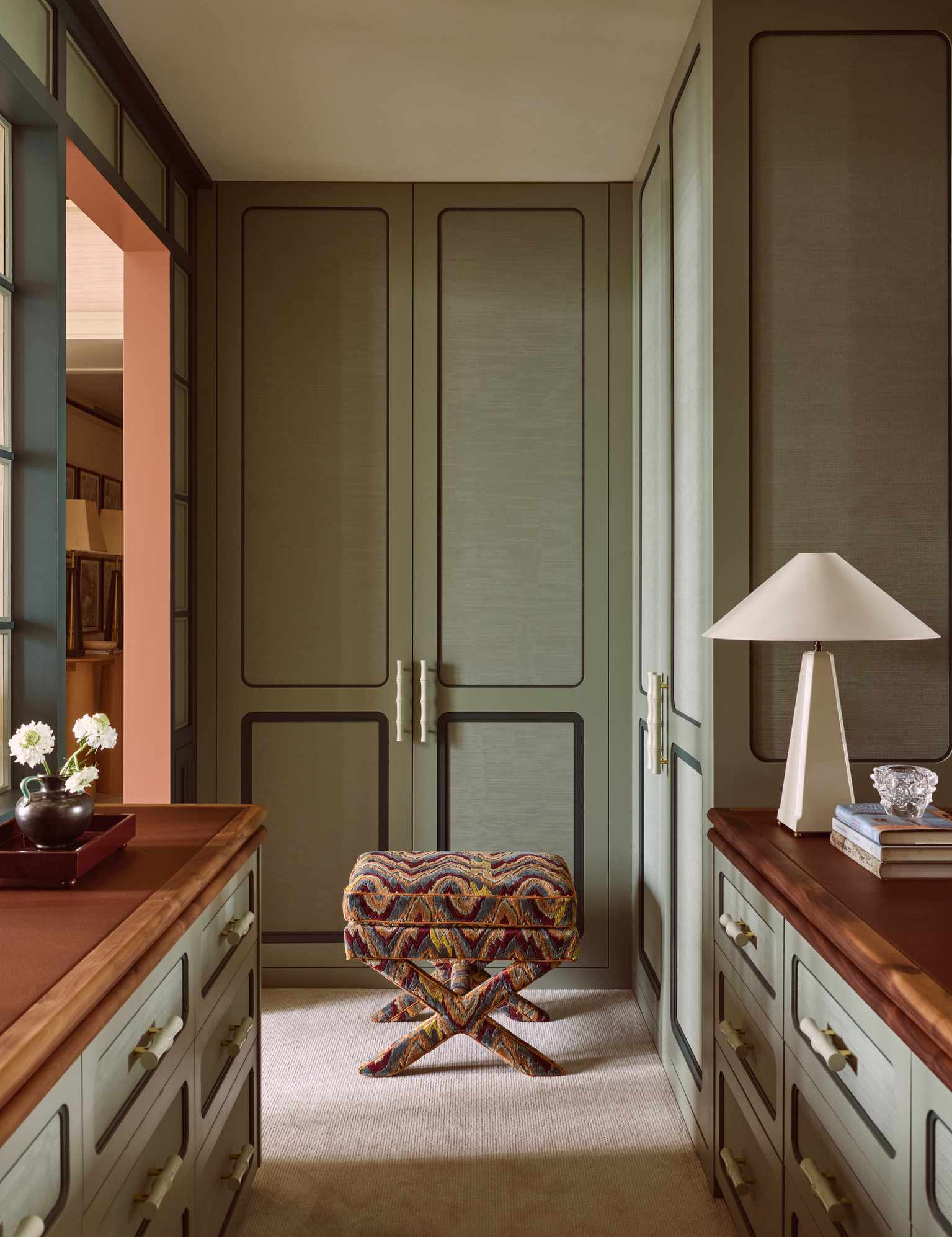 Tranquil dressing room area featuring moss green built-in closet, anchored by a technicolor patterned ottoman and a whisper-light beige carpet