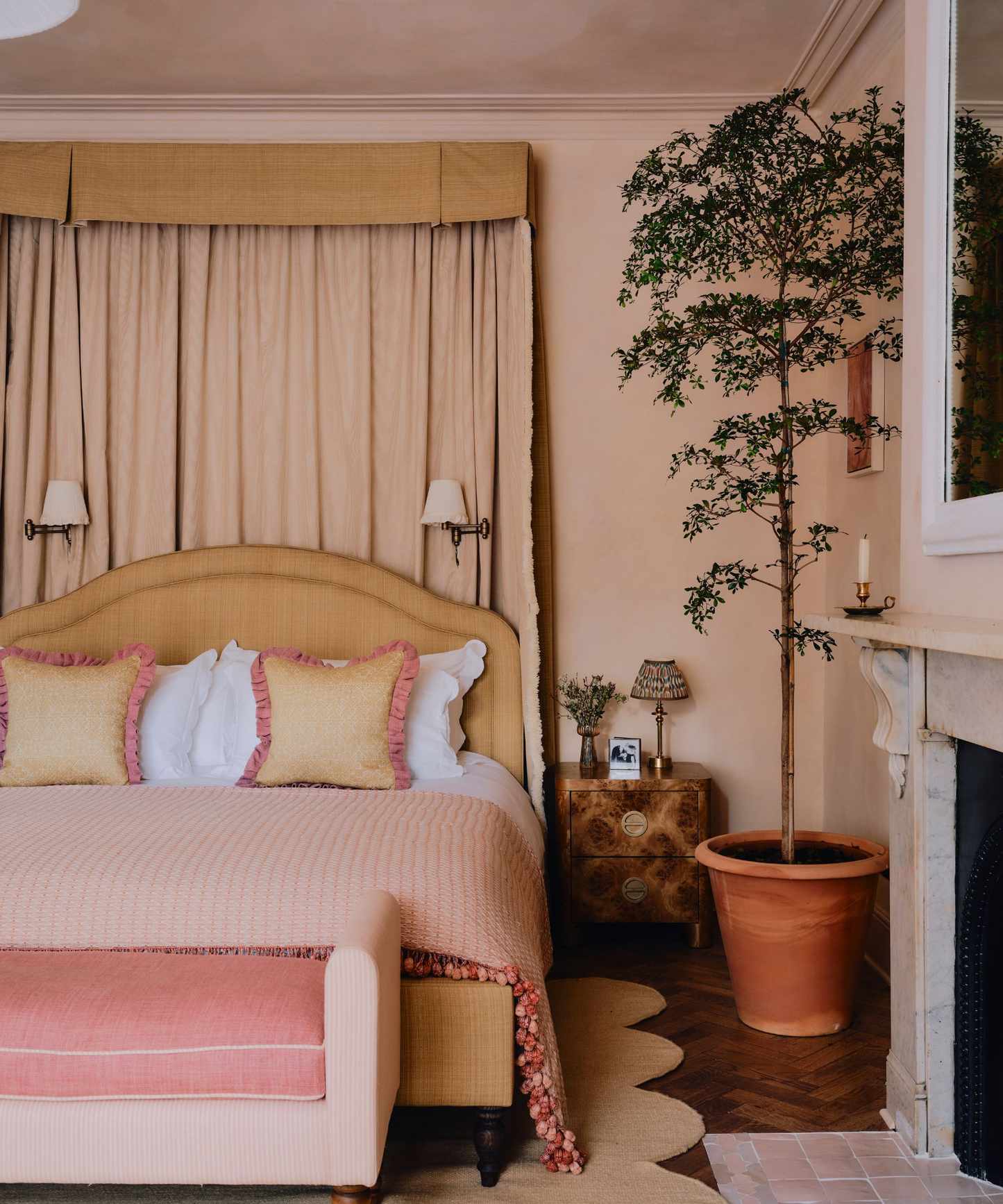 Bedroom with plaster pink walls, wooden parquet floor, large marble fireplace and pink tiles on the floor, a yellow canopy bed, a mustard yellow bed with pink and white bedding and a pink daybed