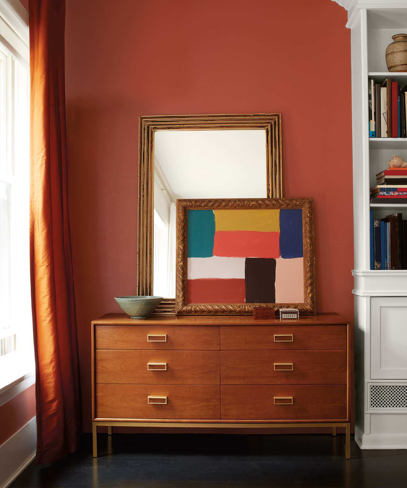 Red painted wall with dark wood cabinet, mirror and artwork sitting atop