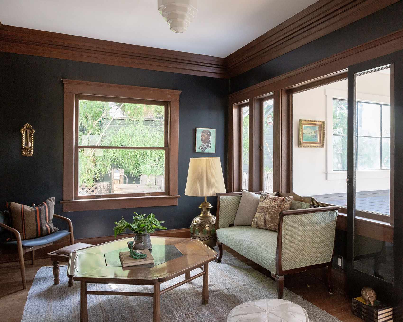 Traditional living room with dark wood detailing on trims, dark wood flooring, gray rug, dark wood coffee table, small sofa and chair with dark wood frame, internal windows looking onto hallway