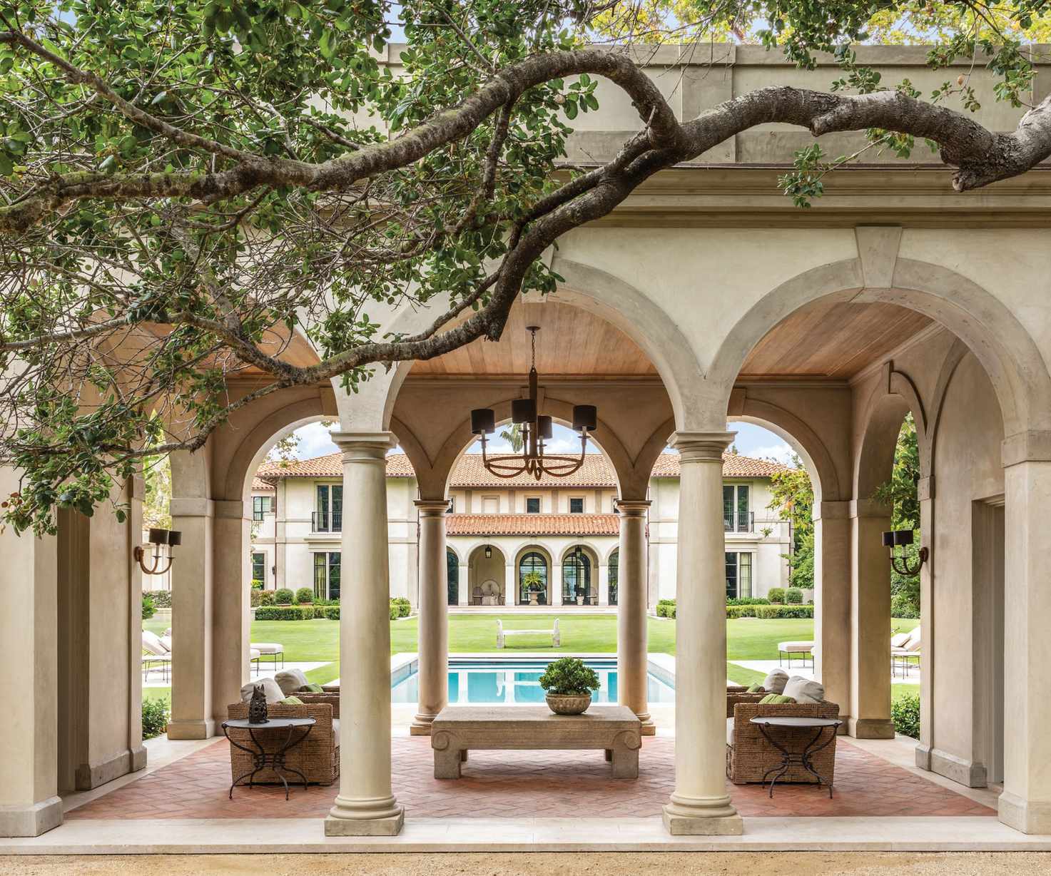 Loggia with arched doorways, terracotta tiled patio, trees and swimming pool