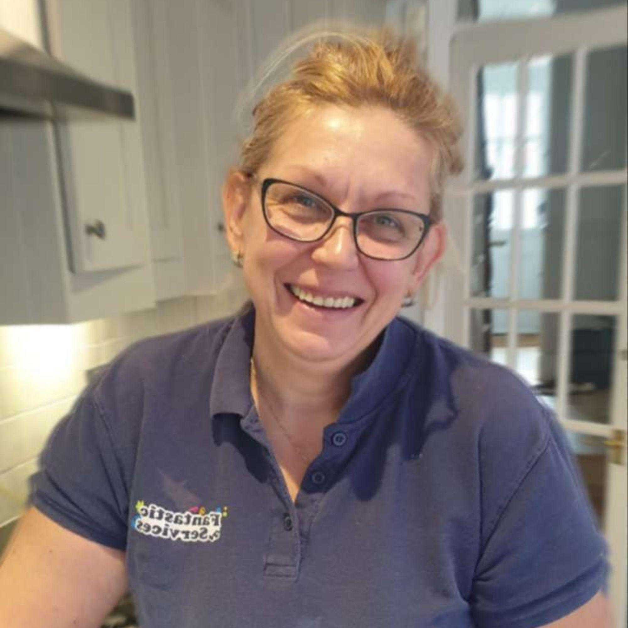 Polya Petrova wears glasses and smiles at the camera in her Fantastic Services uniform