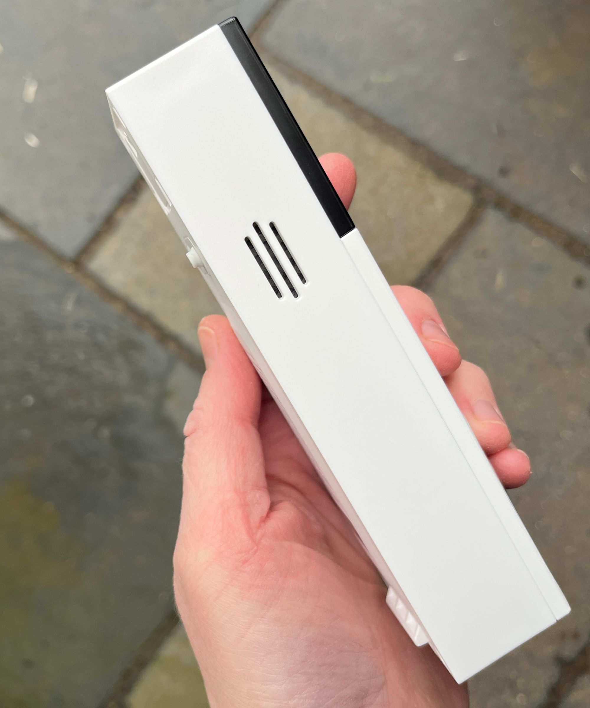 Hand holding the Tapo D210 Video Doorbell, showing the device's side, above tiled concrete floor.