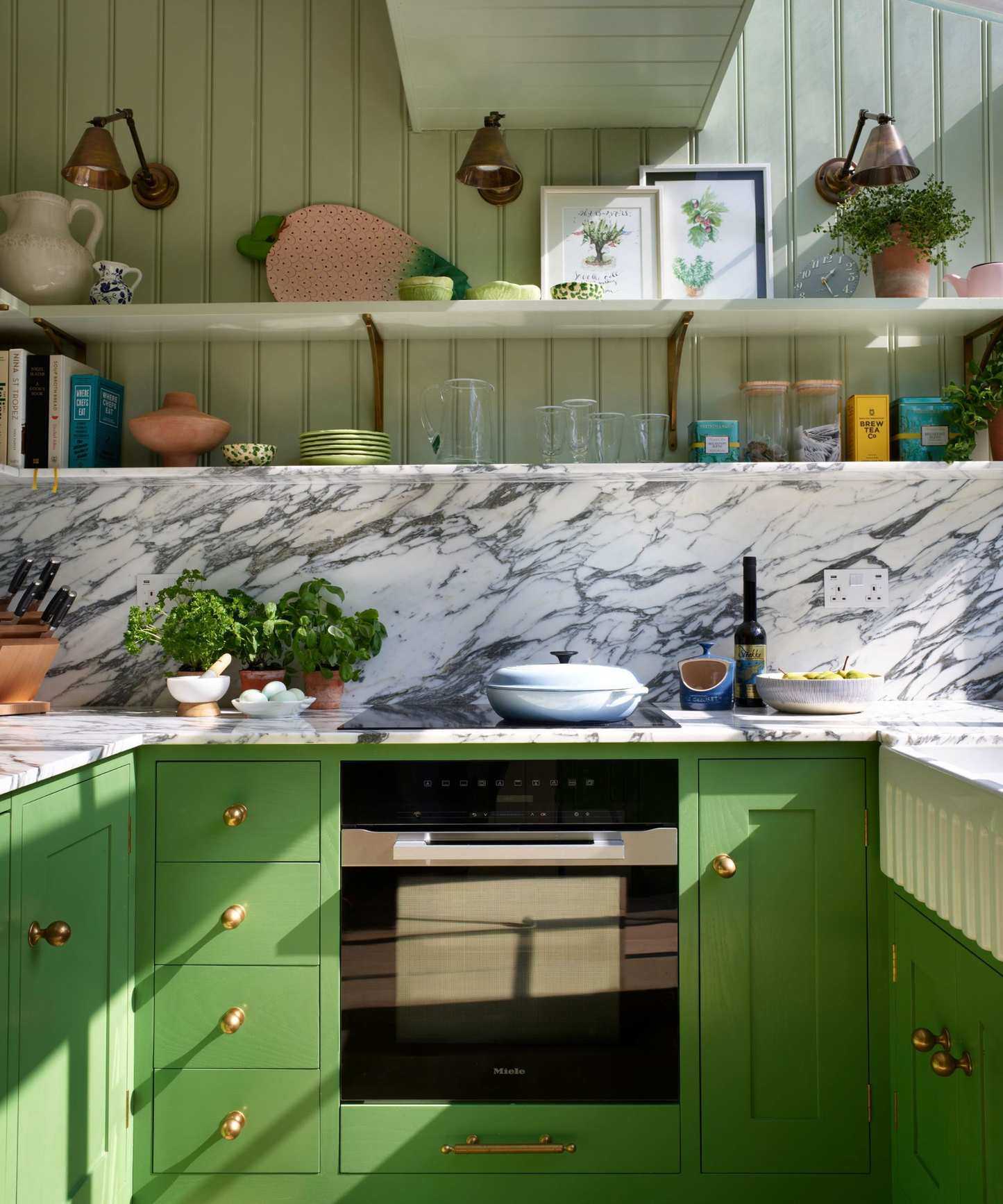 A green kitchen with a marble countersplash and oversized brass hardware