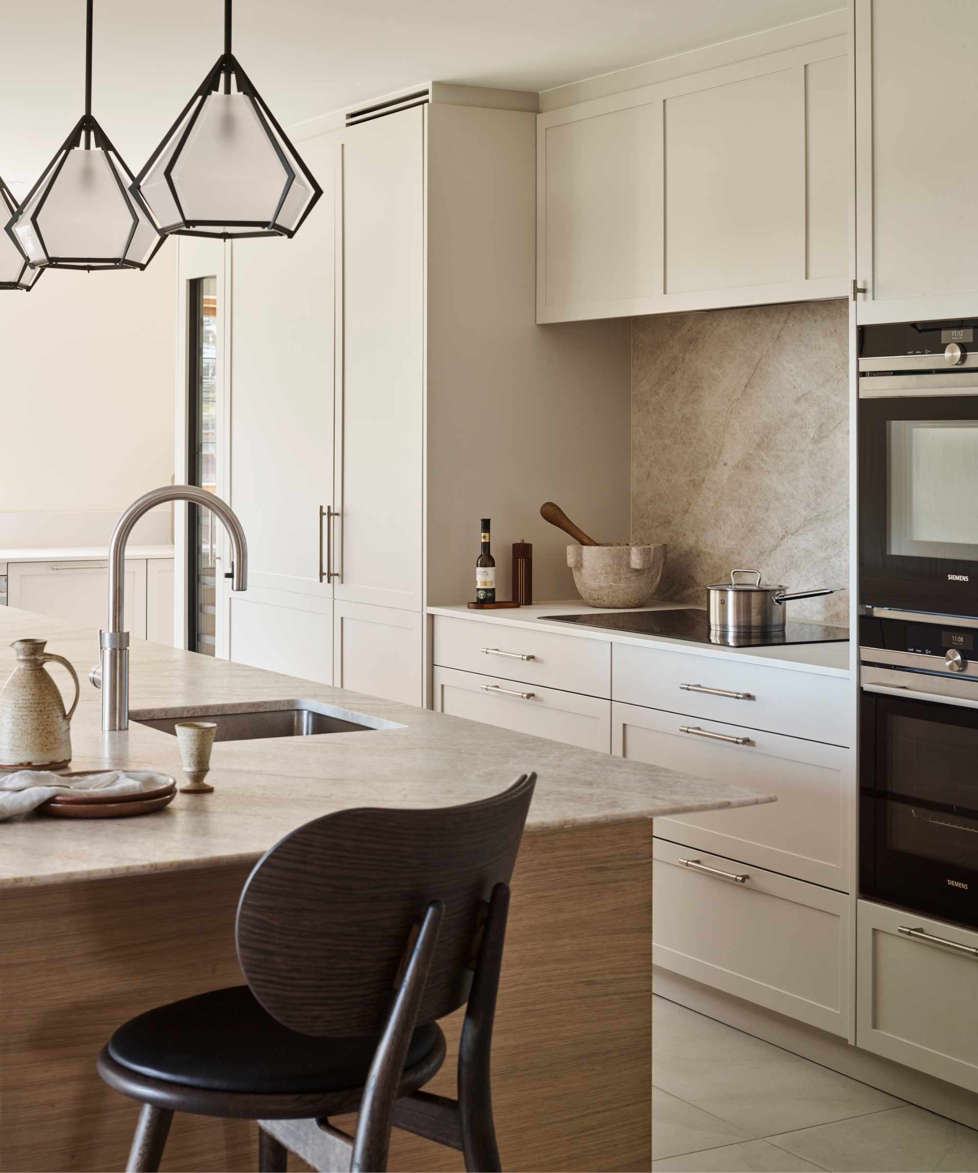 modern minimalist kitchen with white cabinets and counters. natural stone backsplash behind the glass stove top, and a matching stone island