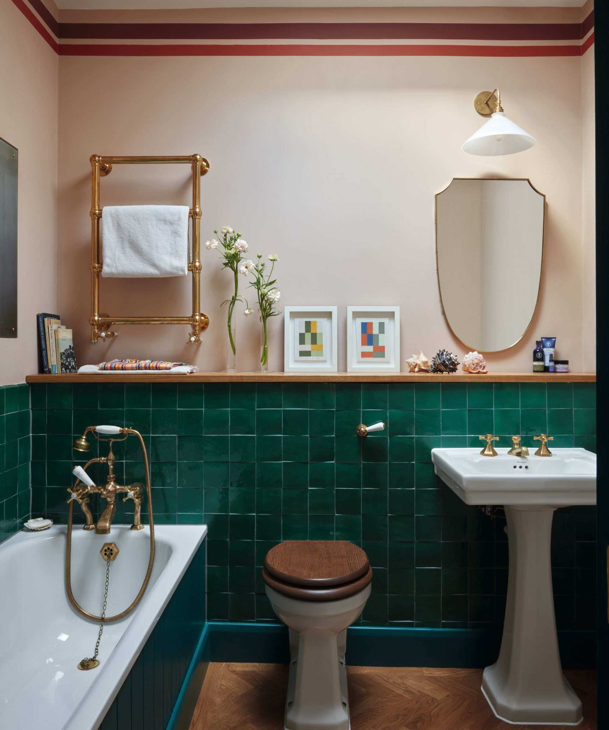 Pale pink bathroom with half the walls tiles in dark green zeillge tiles. The bath is painted to match the tiles and there a gold mirror hanging above the white sink