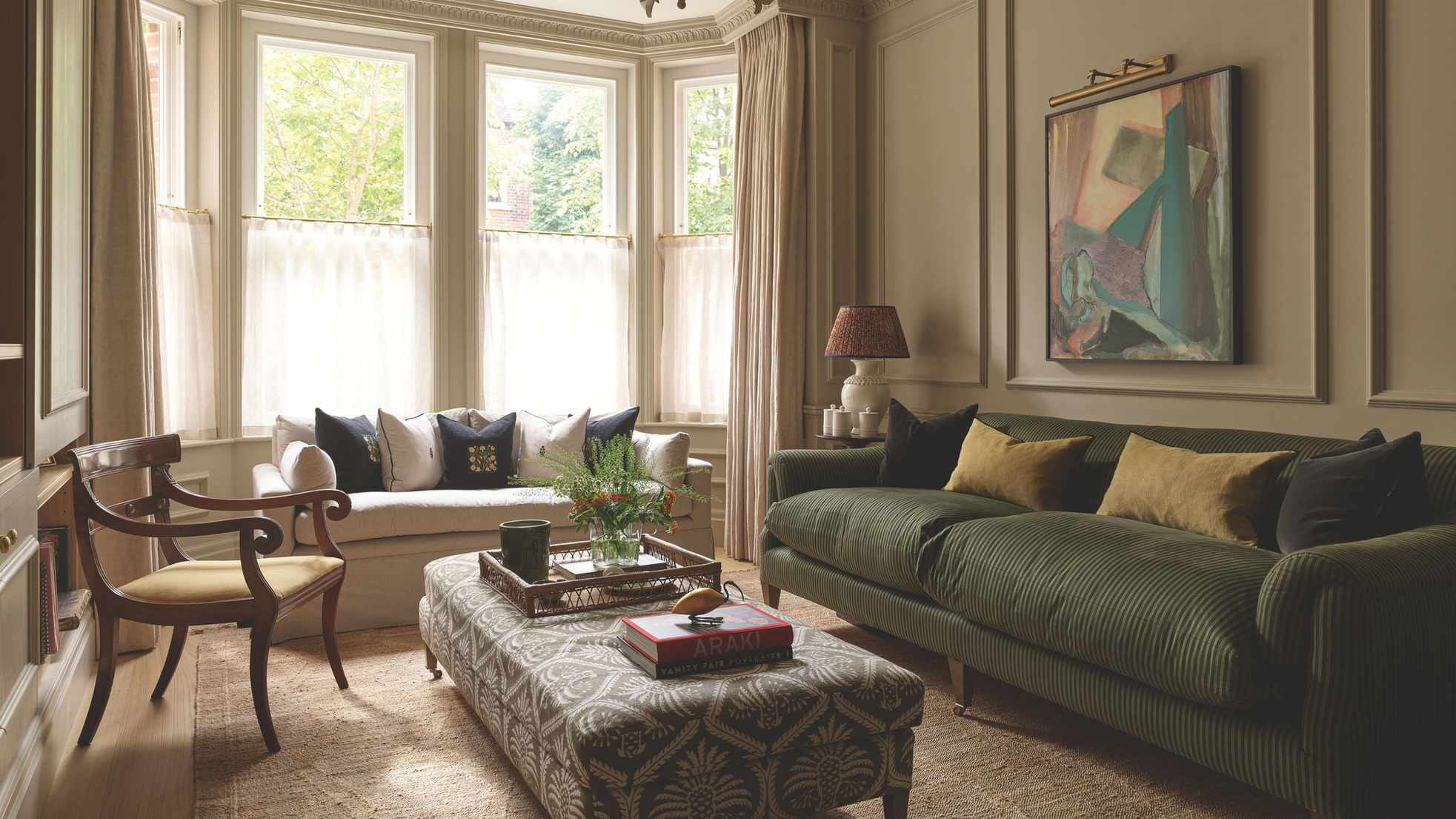 A warm and elegant Georgian living room, featuring a patterned ottoman as a coffee table, two comfy-looking couches and some bold, abstract artwork on the wall