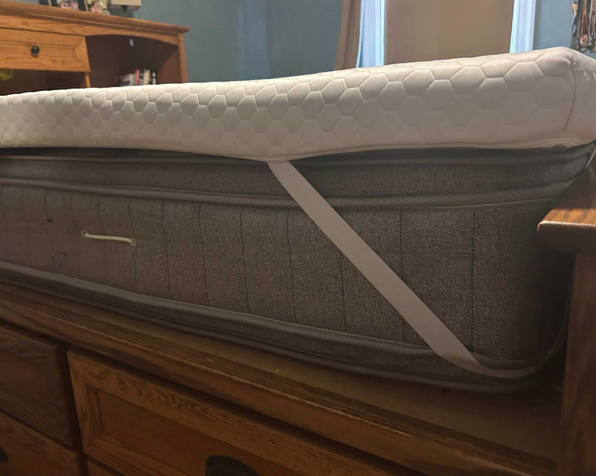 Corner of the white Helix ErgoAlign Mattress Topper on a gray mattress on a wooden bedframe.