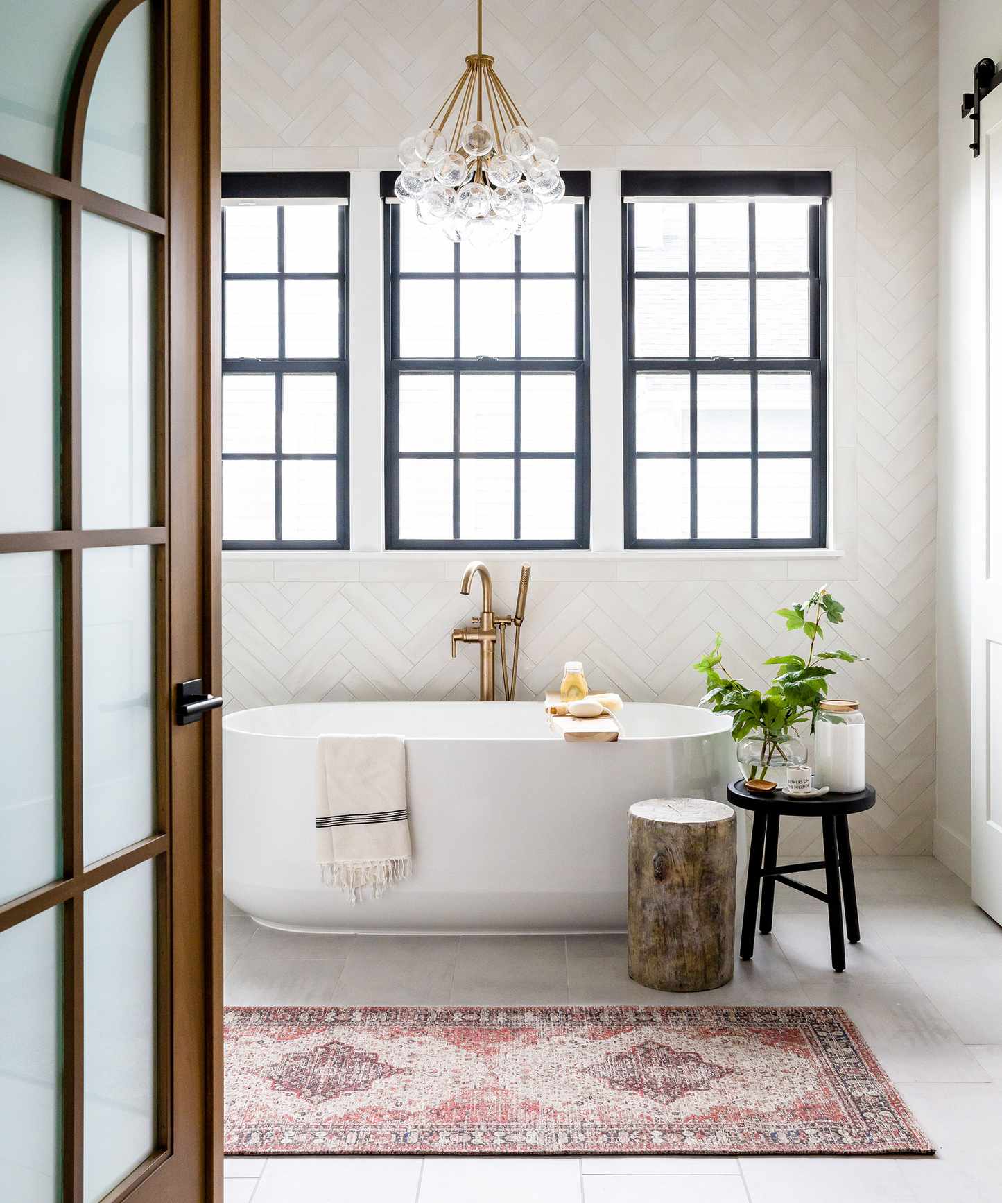 A rolltop bath beneath a window with an oriental rug instead of a bath mat