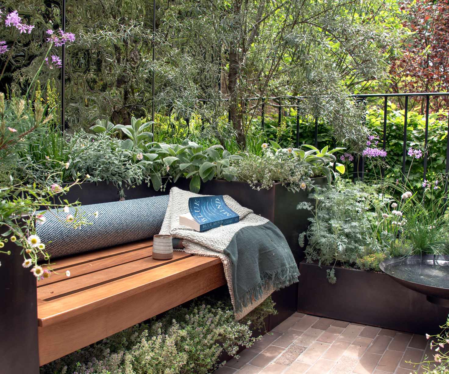 small balcony garden with bench, throw, coffee cup, book and planting