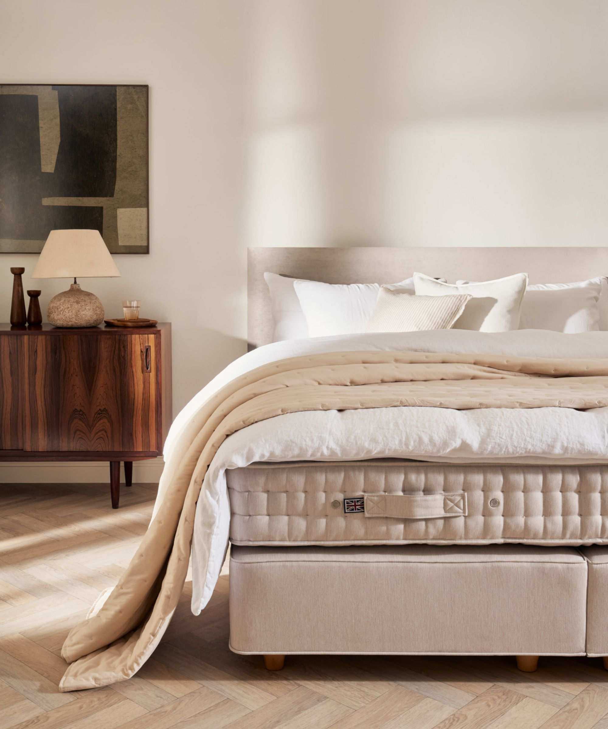 neutral bedroom with an unmade bed showing the mattress, duvet, and pillows with a linen bed frame and mid century room decor