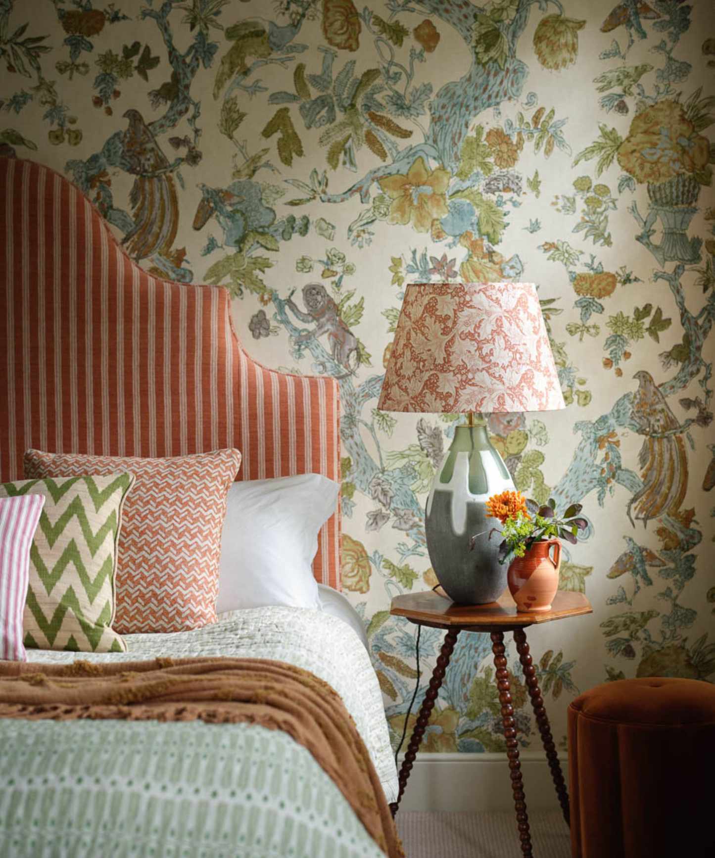 Colourful bedroom with floral wallpaper, striped pink headboard and matching bedding and bedside table with pink patterned lampshade