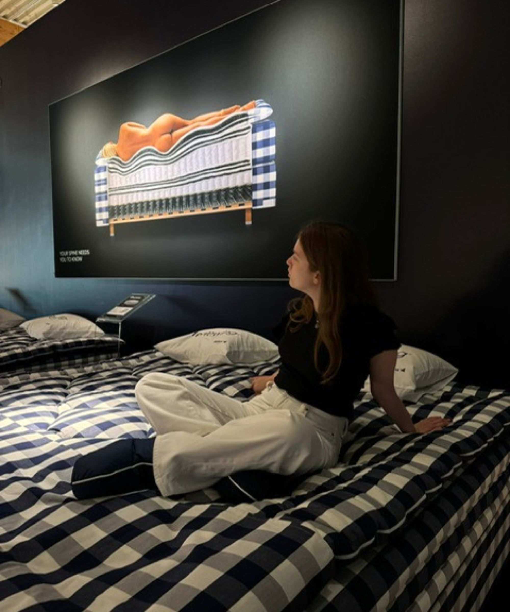 Emilia sitting on a H&auml;stens mattress looking at a poster promoting spinal alignment.