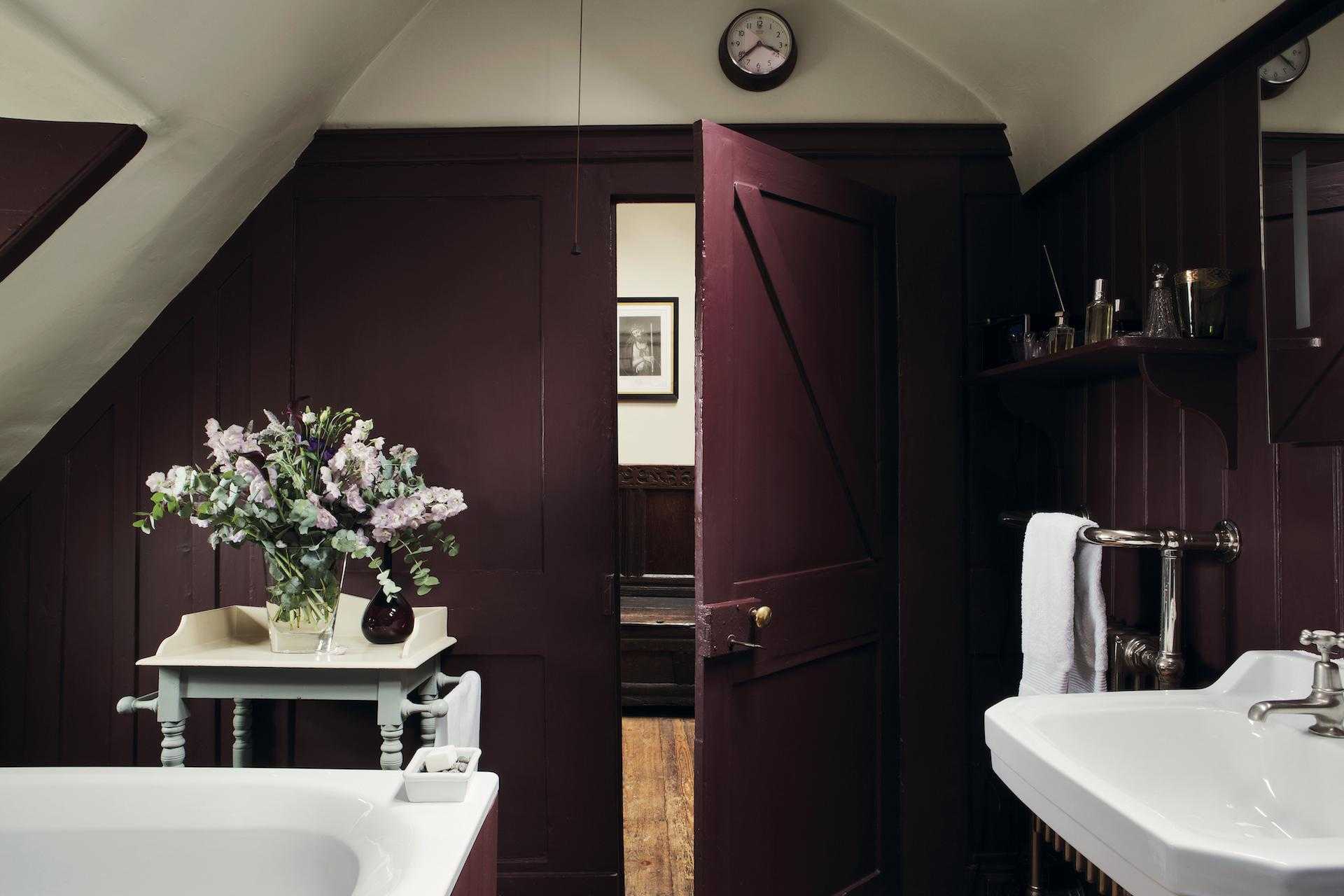 An aubergine colored bathroom in a loft space with wooden panelling and white sanitaryware