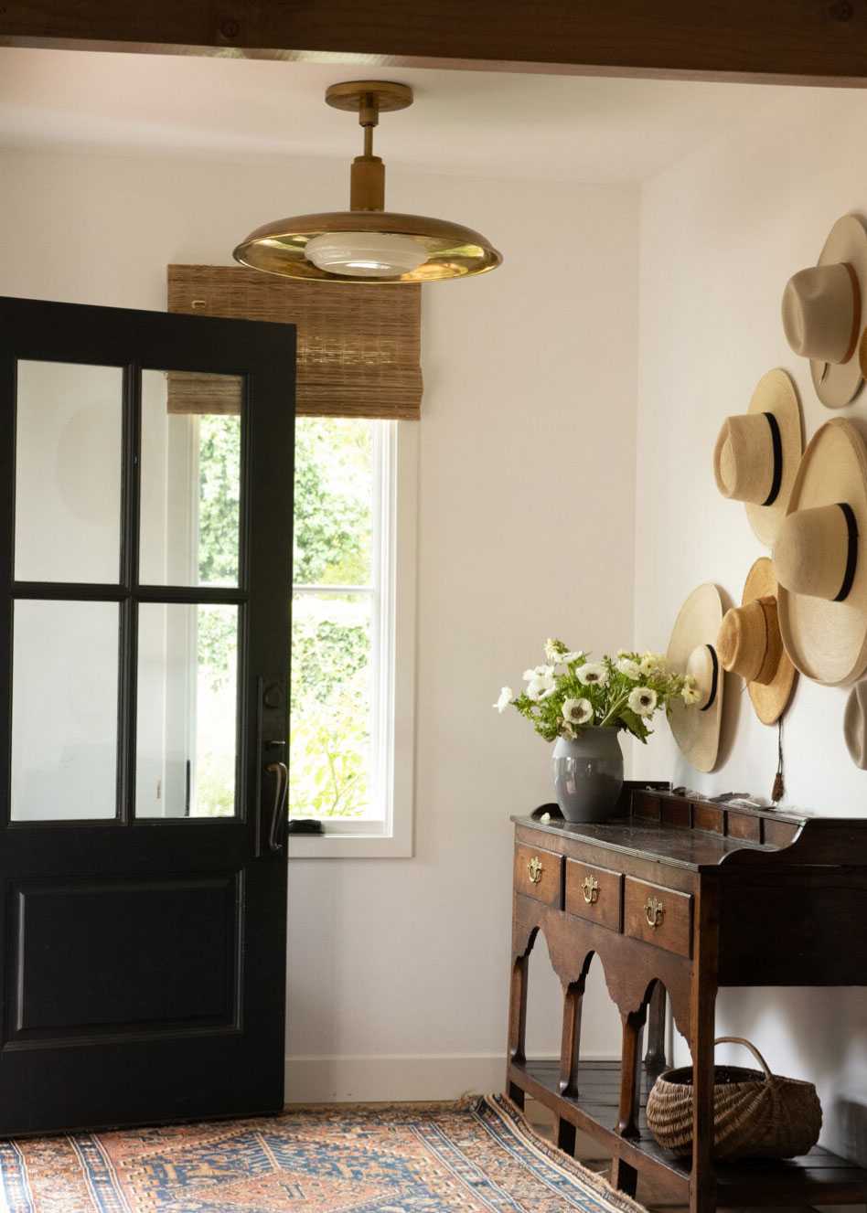 Farmhouse decor ideas, cream painted hallway, patterned rug, blind, wooden console table, straw hats on wall, gold ceiling light