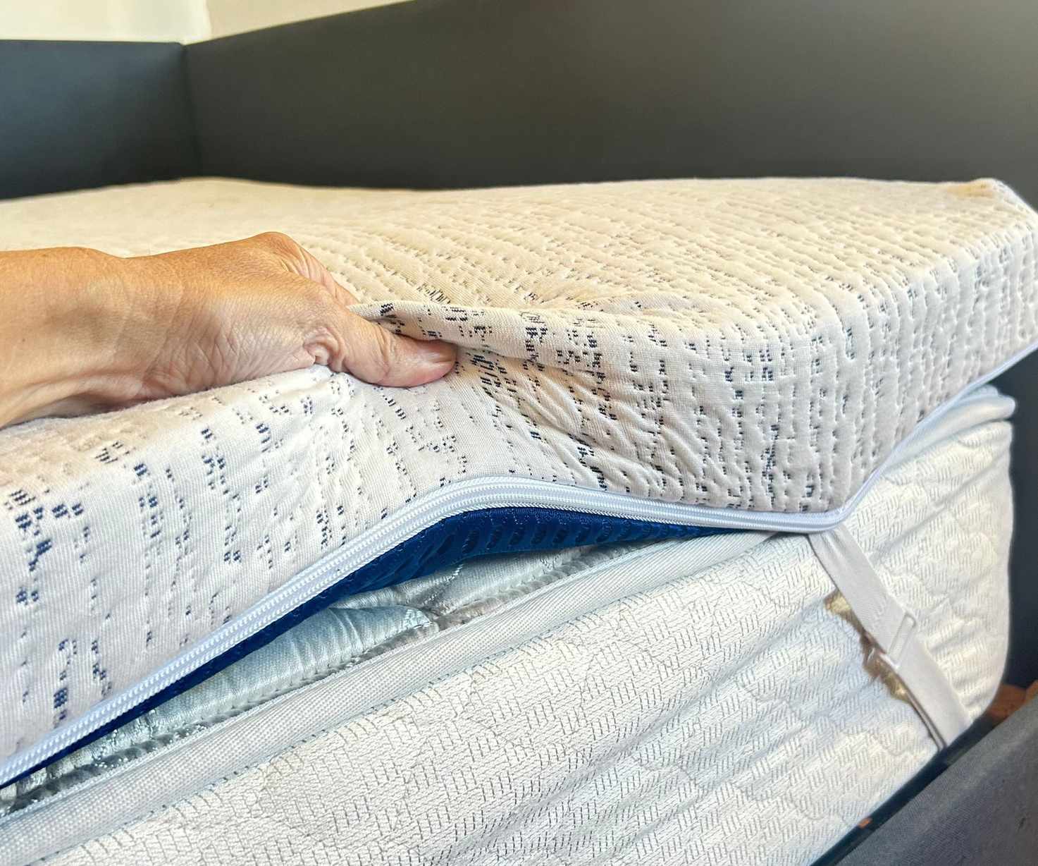 A hand seen squeezing the blue and white Viscosoft High-Density Mattress Topper on a white mattress with white corner straps.