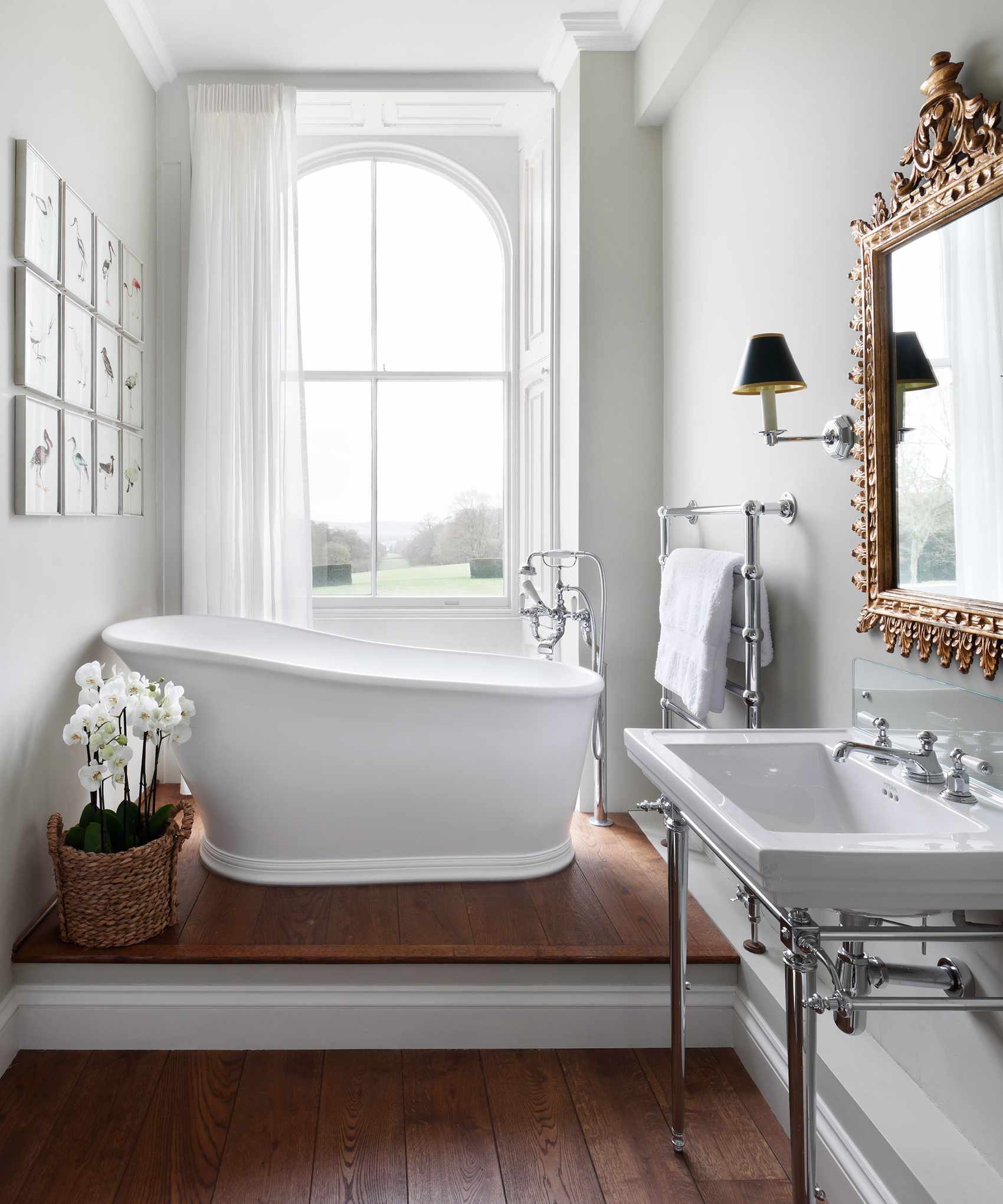 An example of how to make a small bathroom look bigger showing a small bathroom with a small freestanding bath beneath a window with wooden floor
