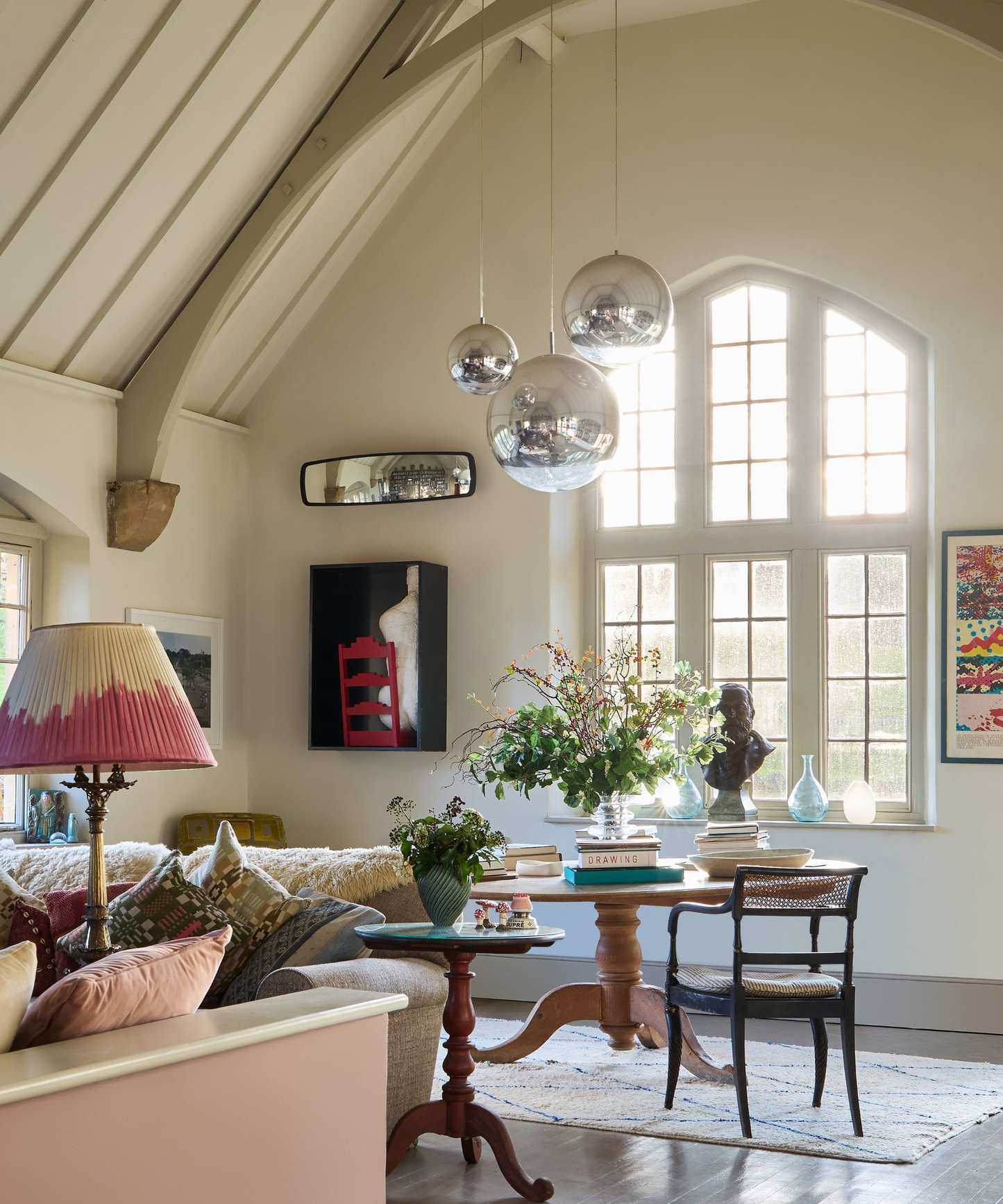 A large room with off white walls and a large window, large silver pendant lights hang from the ceiling