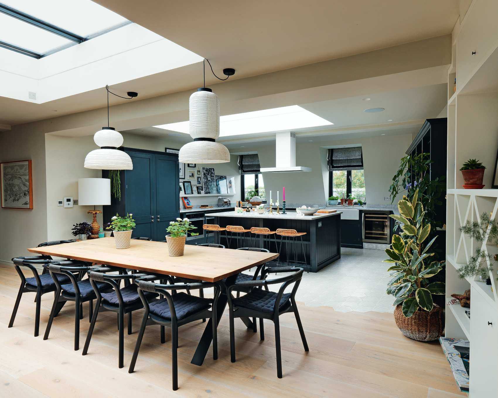 Open plan kitchen in a room with white walls, skylights, a large wooden table and dark blue cabinetry.