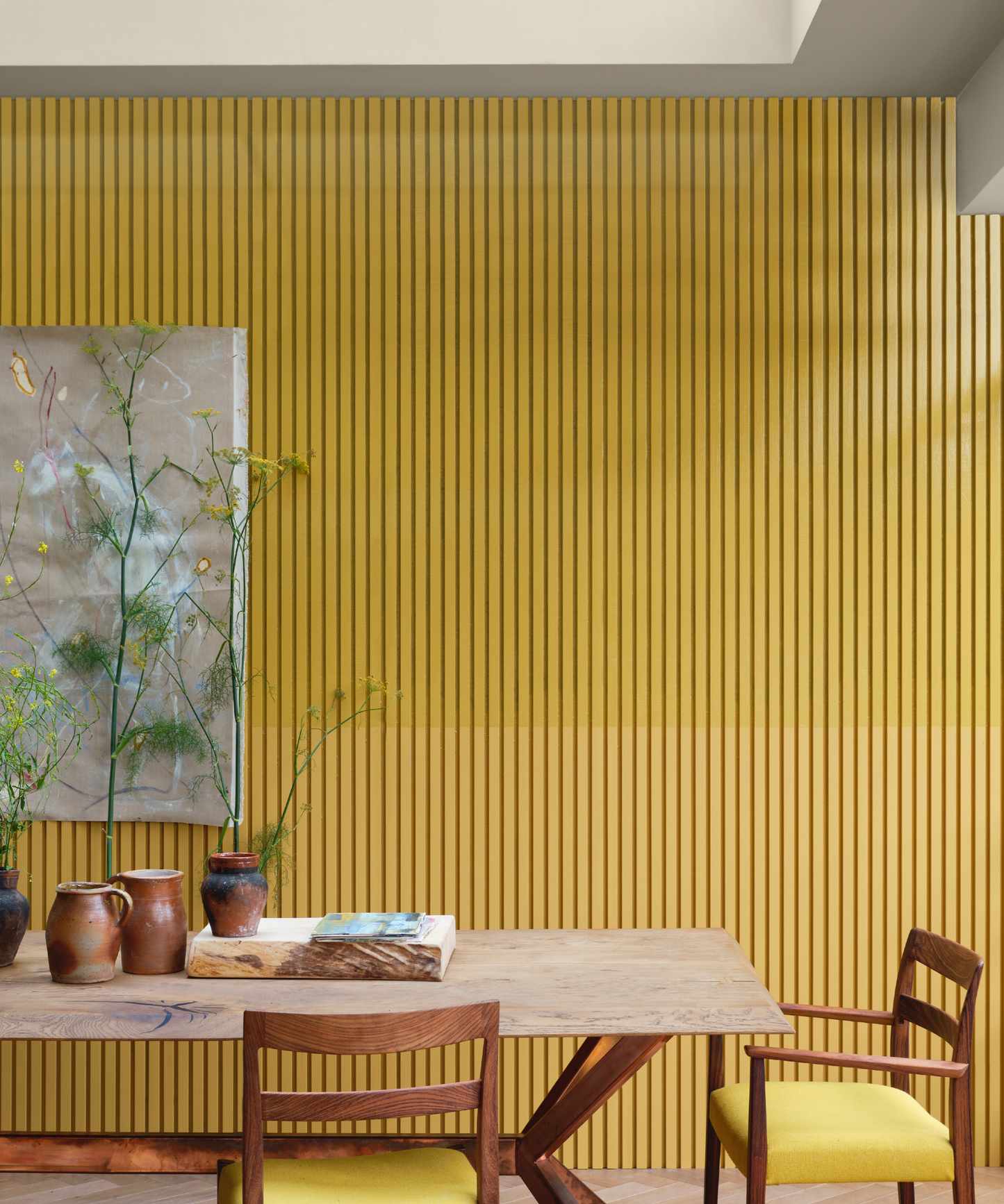 yellow dining room with painted slatted wall behind, artisan style table and chairs, earthenware on table, artwork