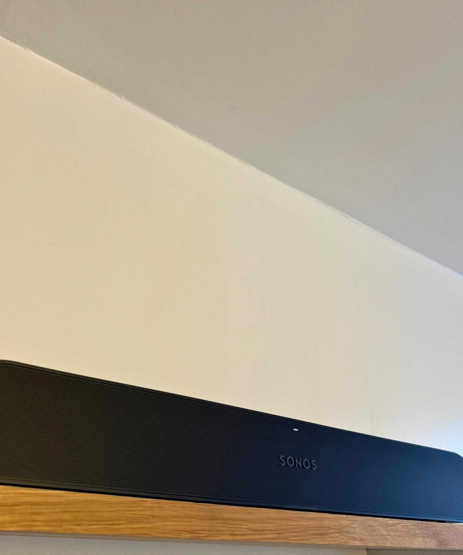 The Sonos Ray soundbar on a wooden shelf in front of cream-white wall.