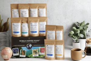 Brown bags of coffee beans are stacked on a gift box. At right, a cup of coffee sits in front of a potted succulent. 
