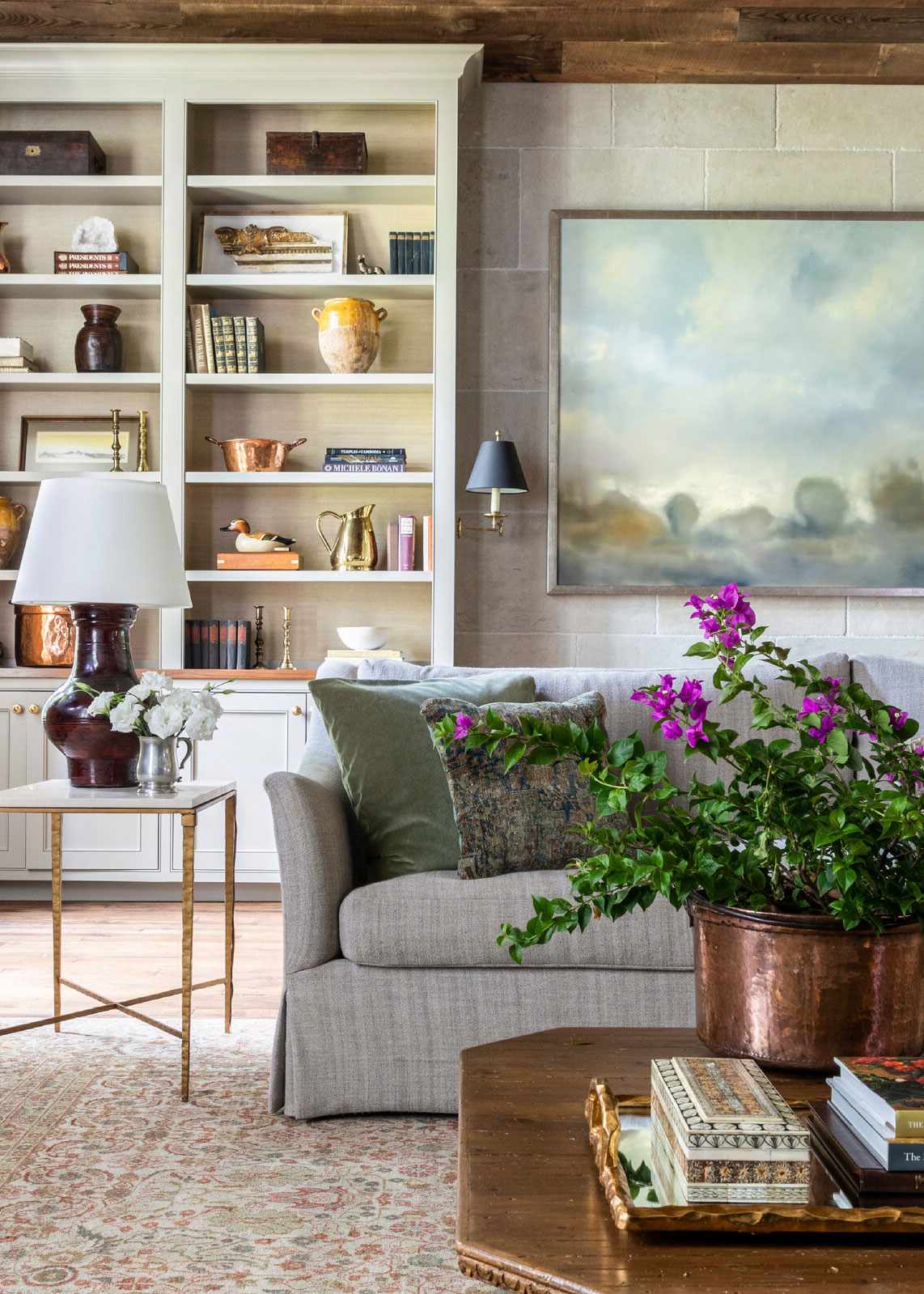 Farmhouse decor ideas, cozy living room with patterned rug, gray sofa, wooden coffee table, white shelving, large artwork
