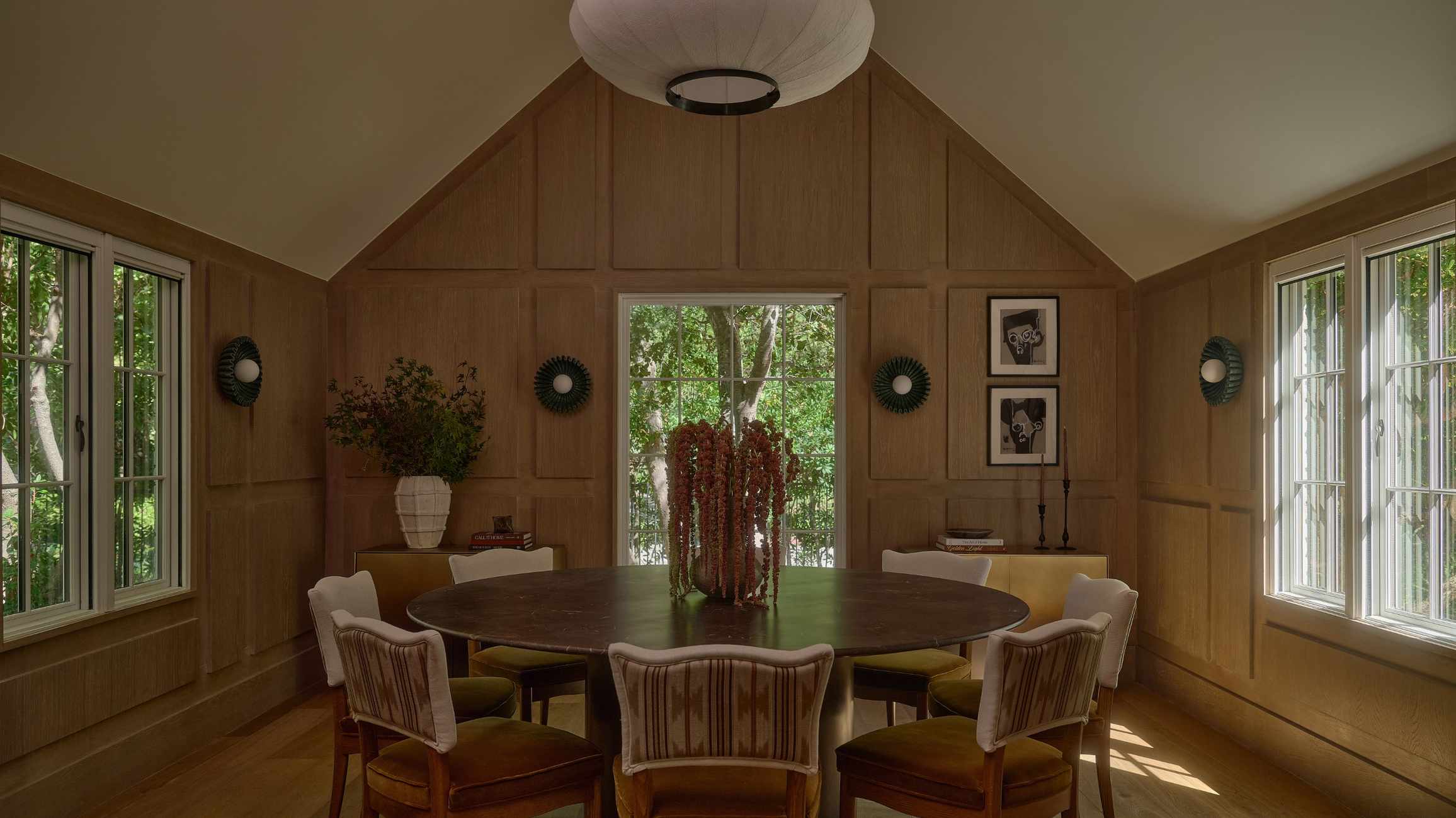 a wooden clad dning room with paneled walls and a vaulted ceiling with a large round table