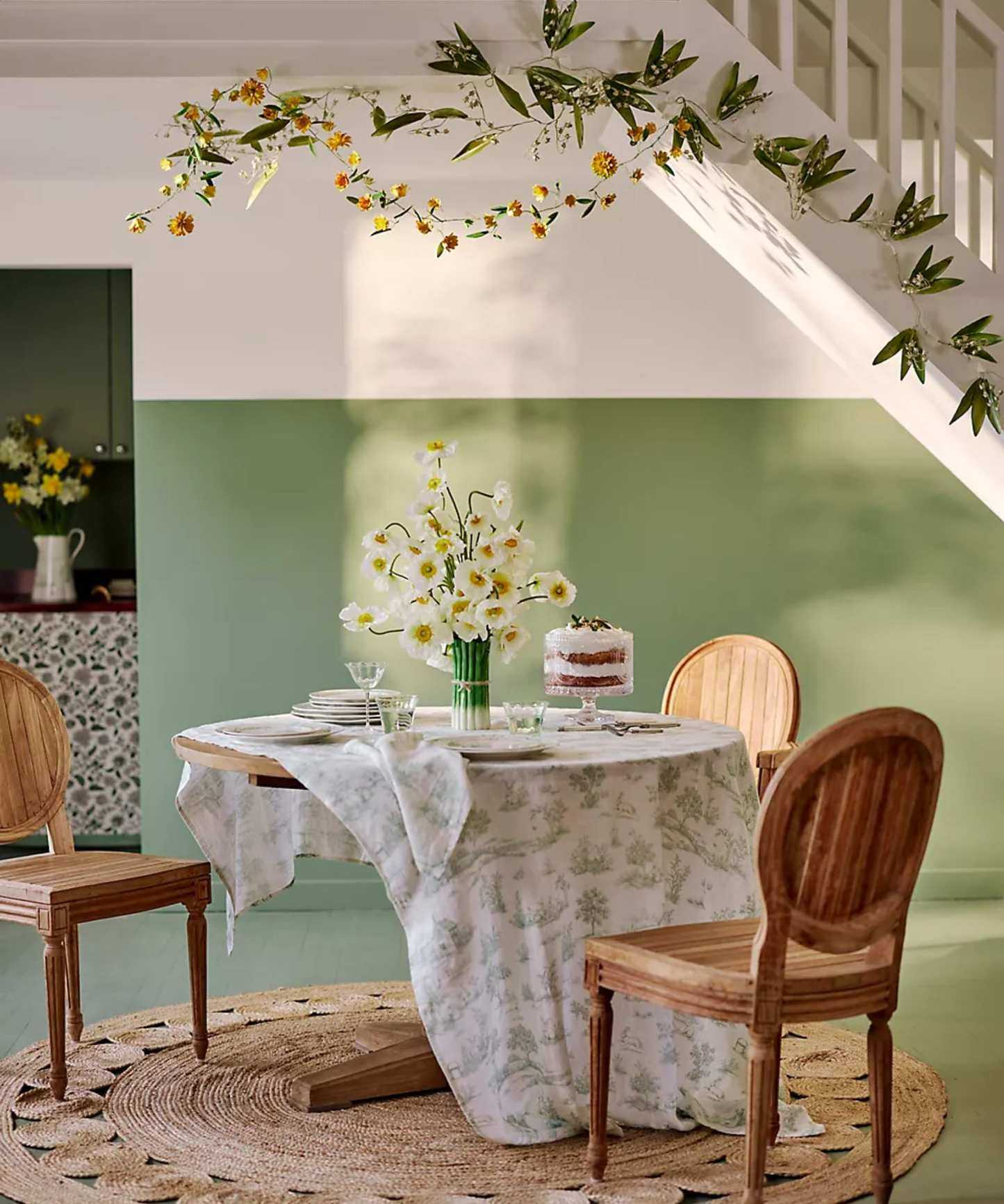 a white and green dining room with a staircase draped with spring garlands