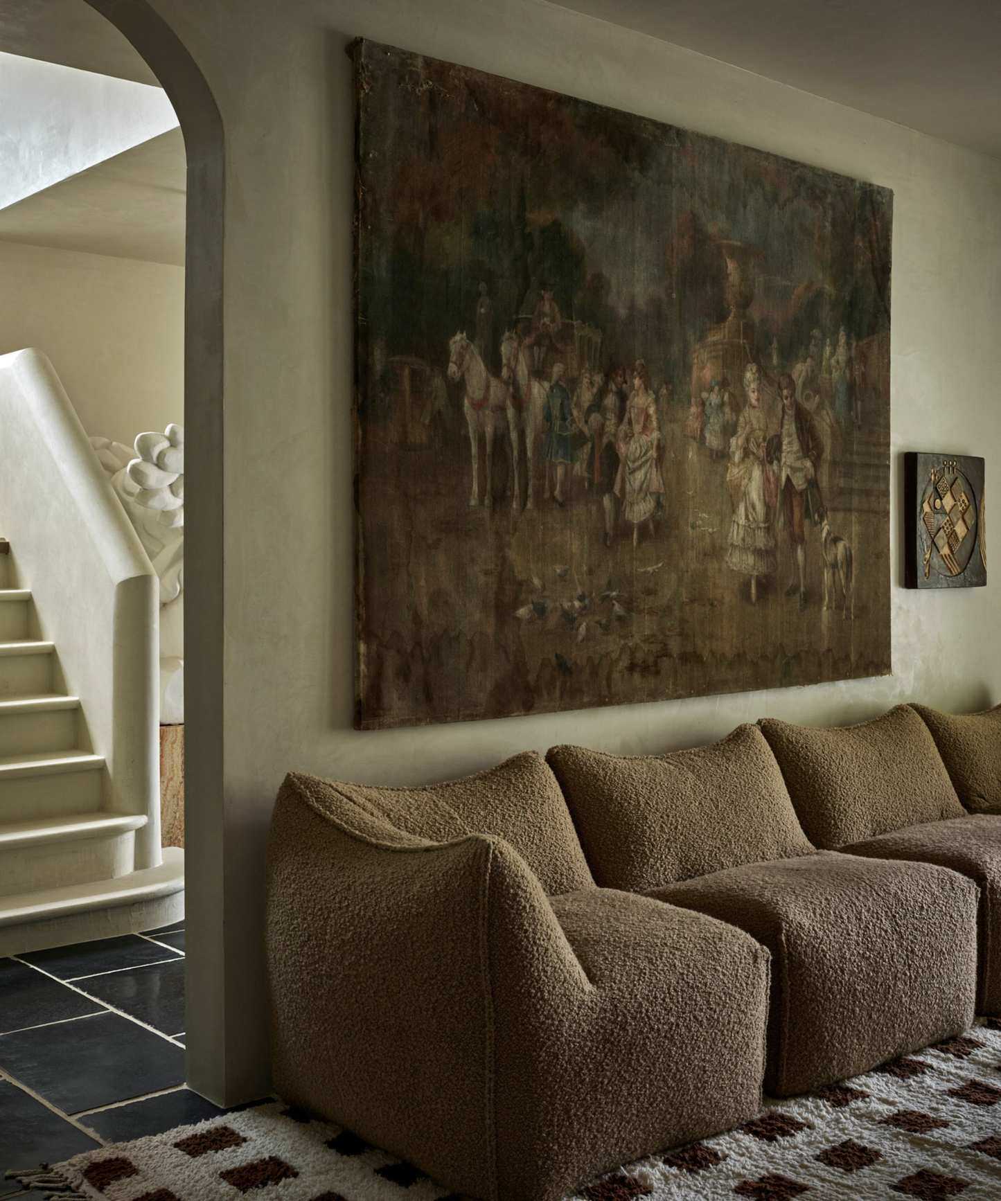 modern living room with limewash walls, a low boucle sofa, checkered rug and large vintage wall art