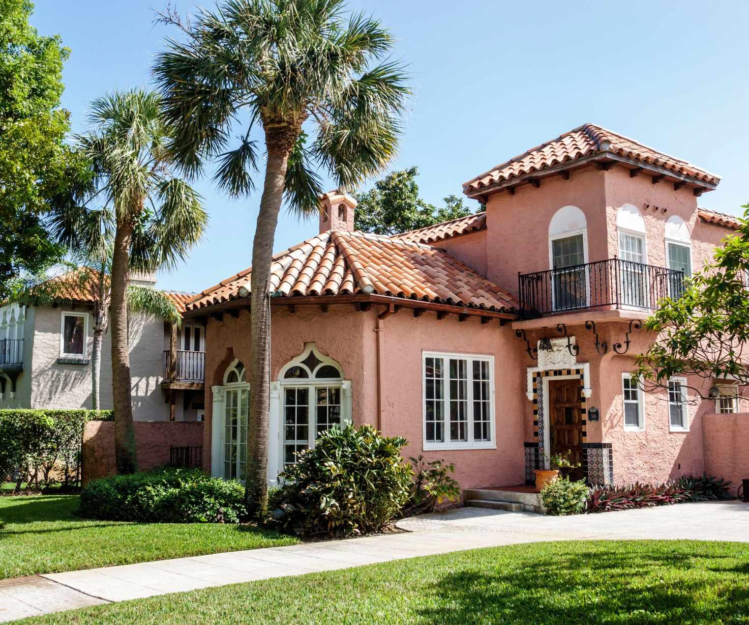 Tuscan style house with peach-painted exterior, wrought iron balconies, curved windows with shutters and palm trees