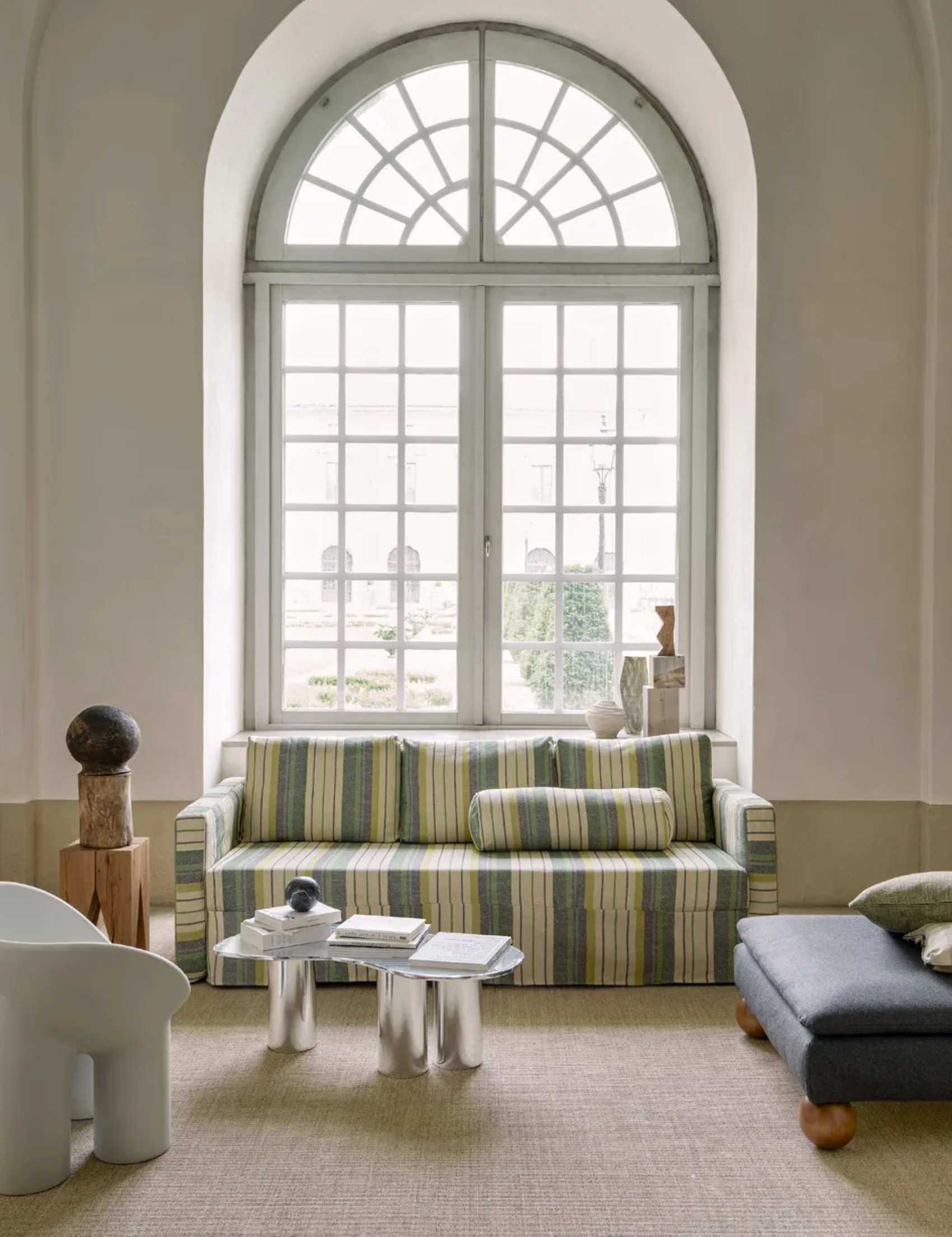 Modern living room design in traditional interior, sofa with striped upholstered covers, armchairs and lounge chairs working with sofa to create a sociable seat space, large arch window