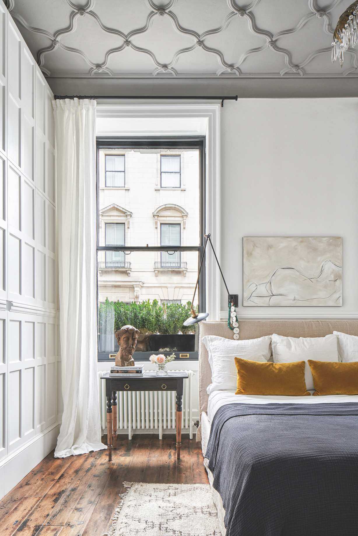 white bedroom with black accents, wooden floor, black throw, mustard cushions, wall light, artwork, decorative ceiling, panelled walls, desk