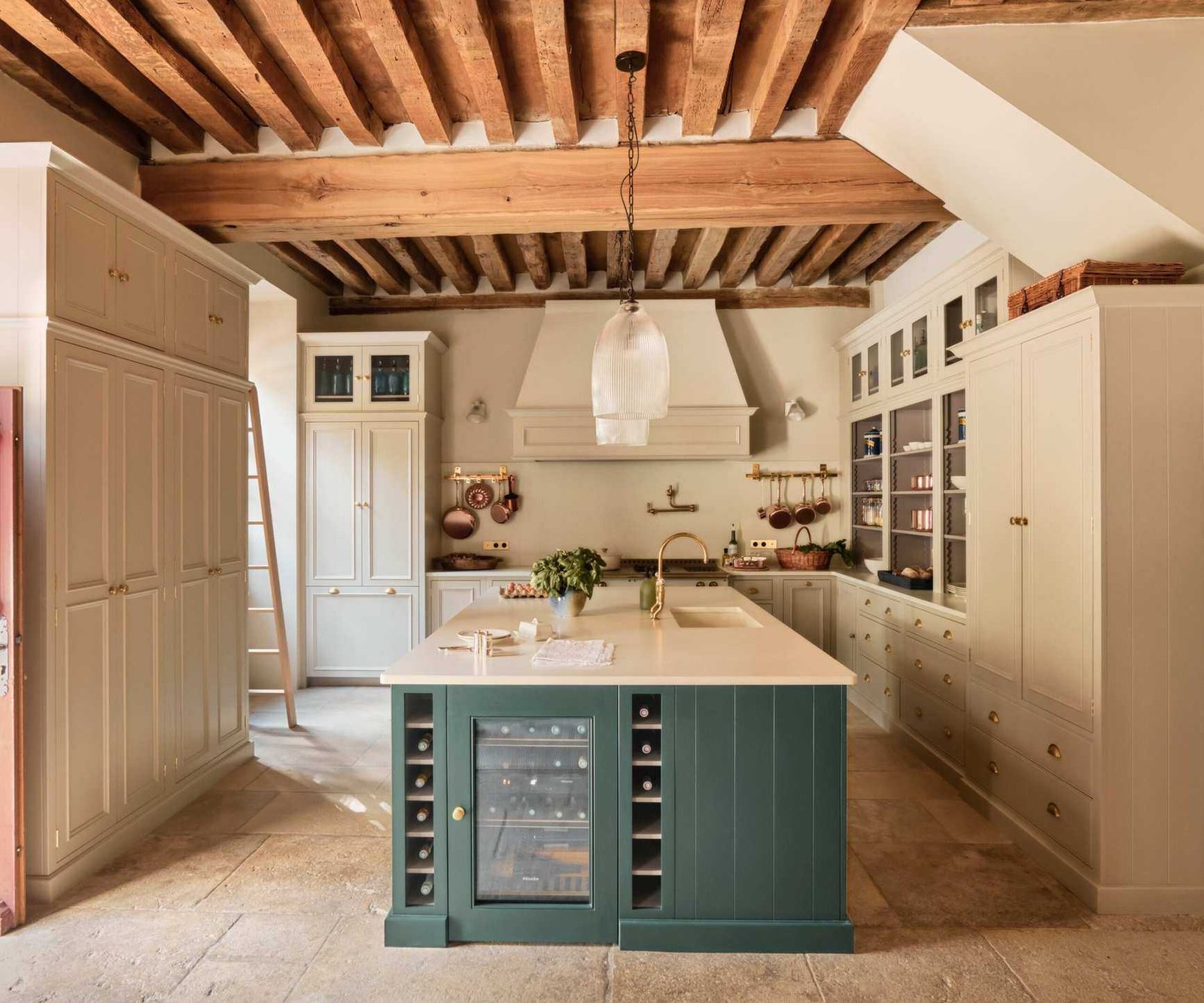 A traditional kitchen with white cabinets, a green island featuring wine racks and a drinks fridge, and exposed ceiling beams