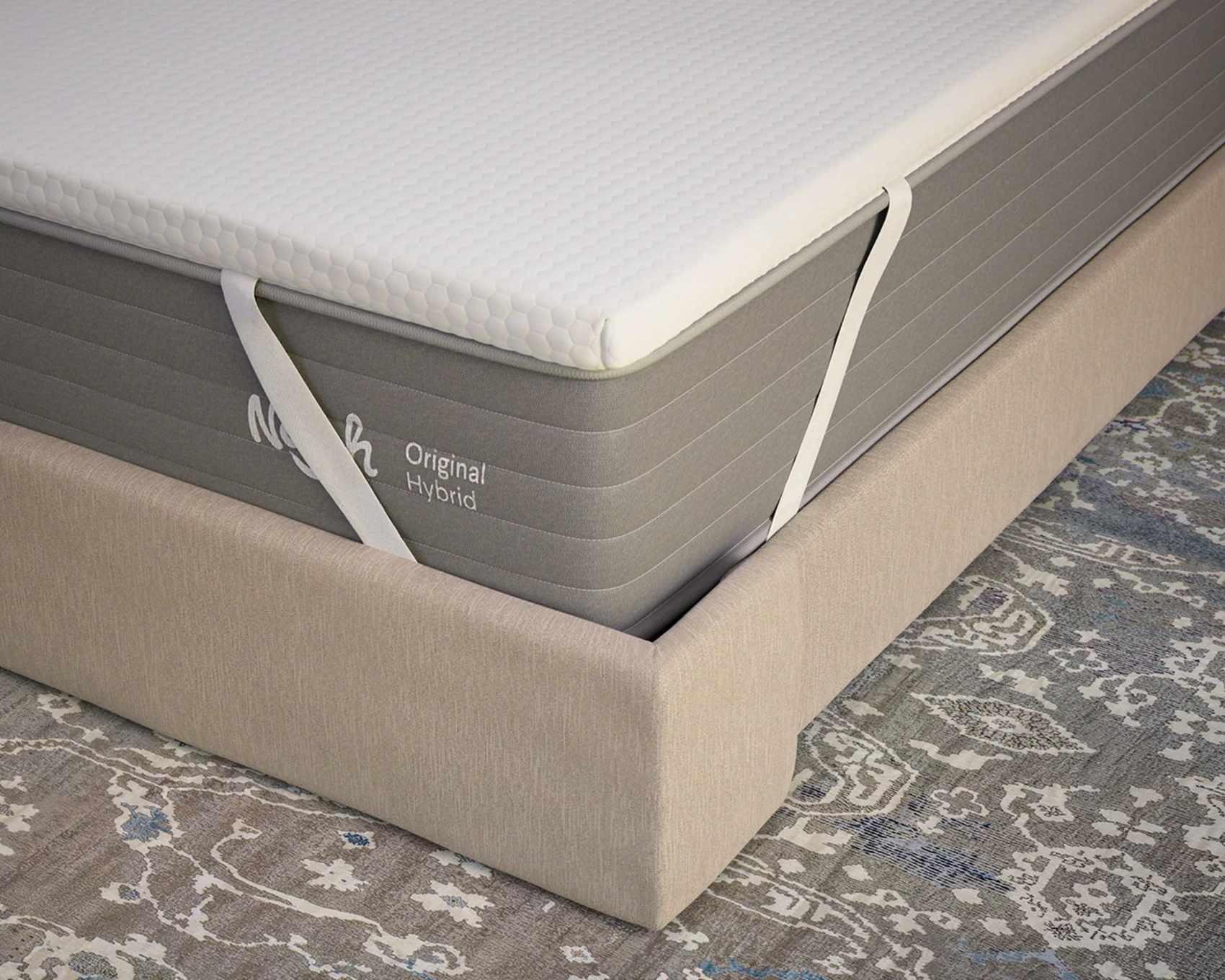 Nolah AirFoam® Luxe Mattress Topper on a grey Nolah Original Hybrid mattress, shown on a beige bed frame on top of a grey patterned Persian-style rug.