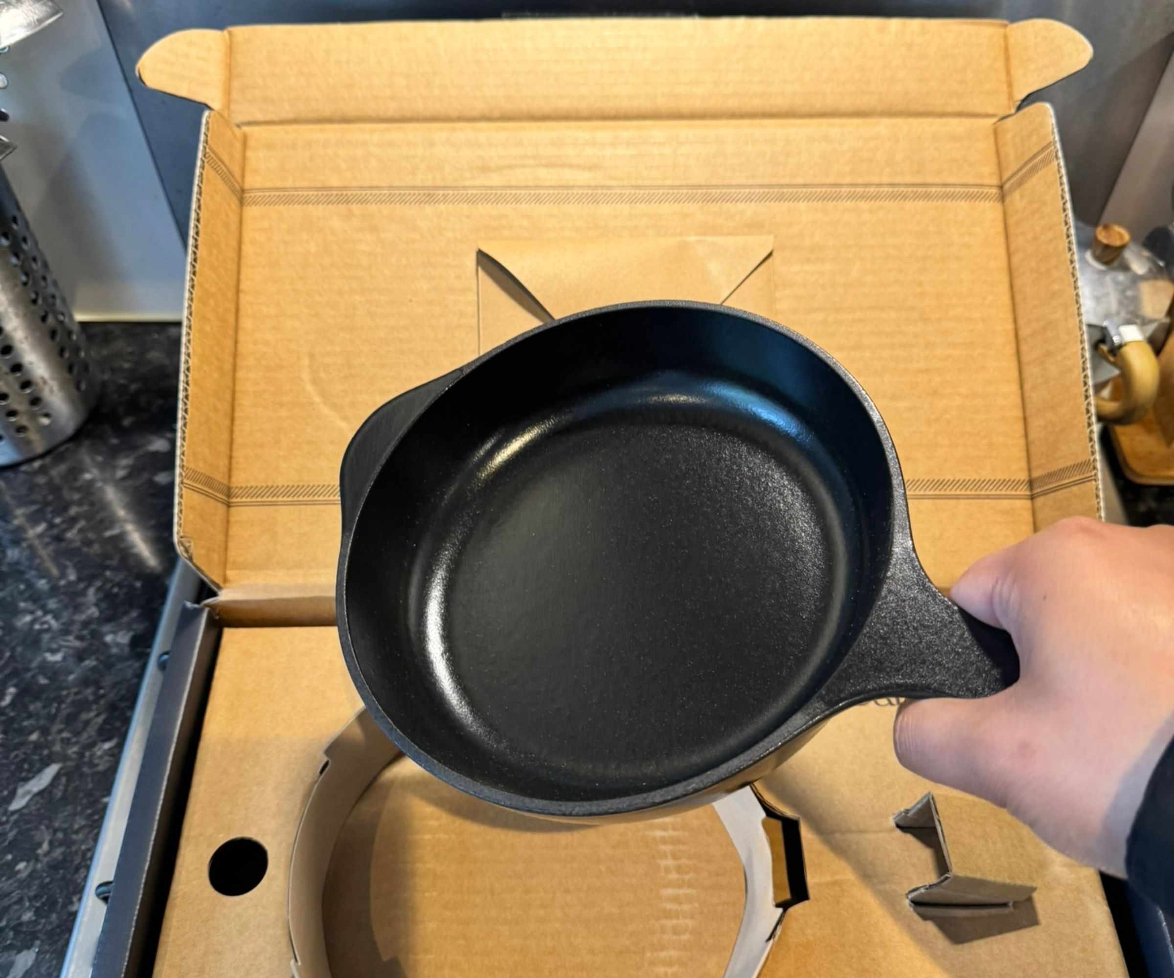 Someone holding the Caraway mini cast iron skillet above the box.