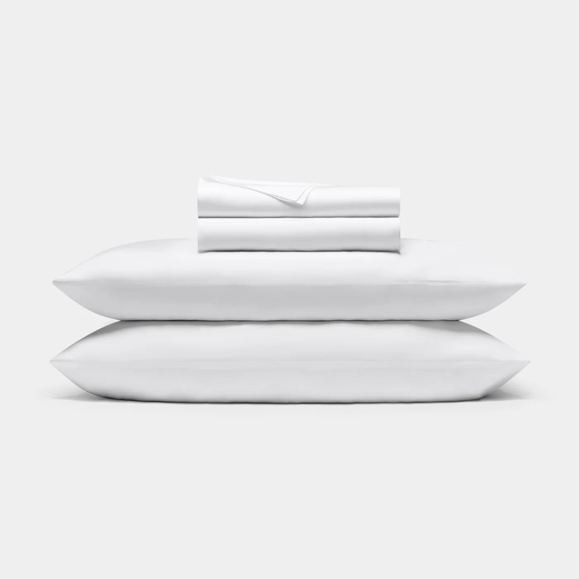A white pillowcases shown on two piled pillows with folded sheets on top.