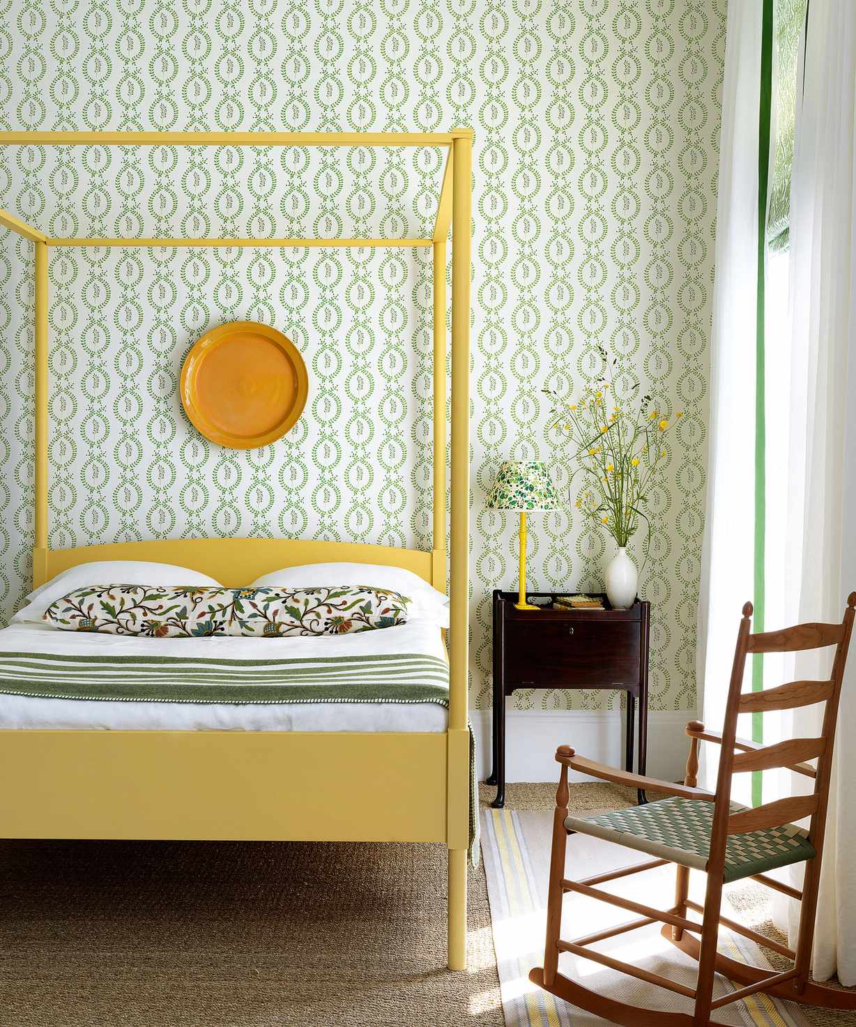 A yellow four-poster bed in front of a wall with green and white patterned wallpaper