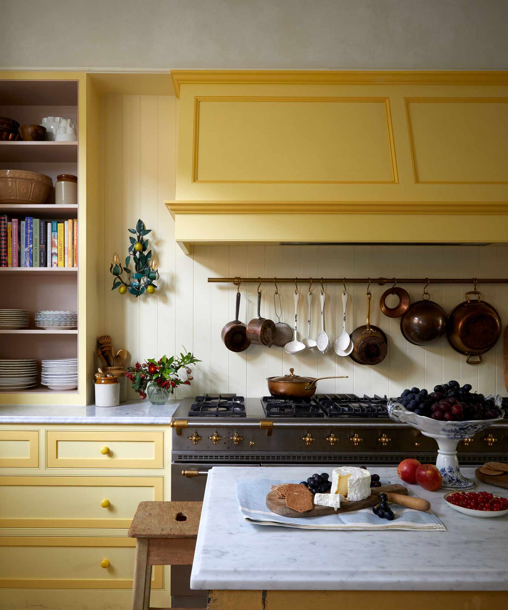 Kitchen with yellow units, cream walls, parquet flooring and large range cooker with saucepans hanging on the wall above.