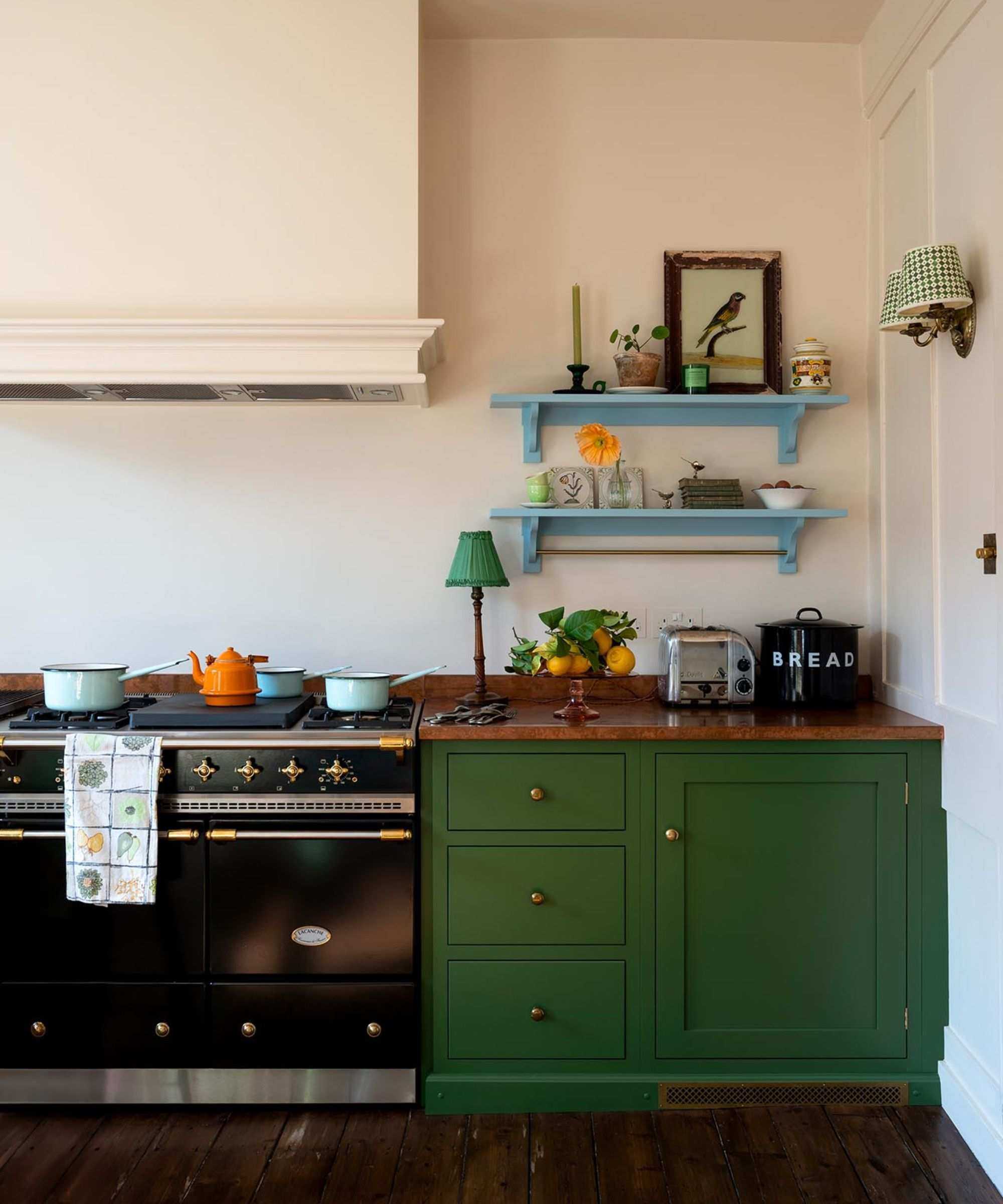 A small green kitchen with copper countertops and two blue floating shelves filled with vintage decor