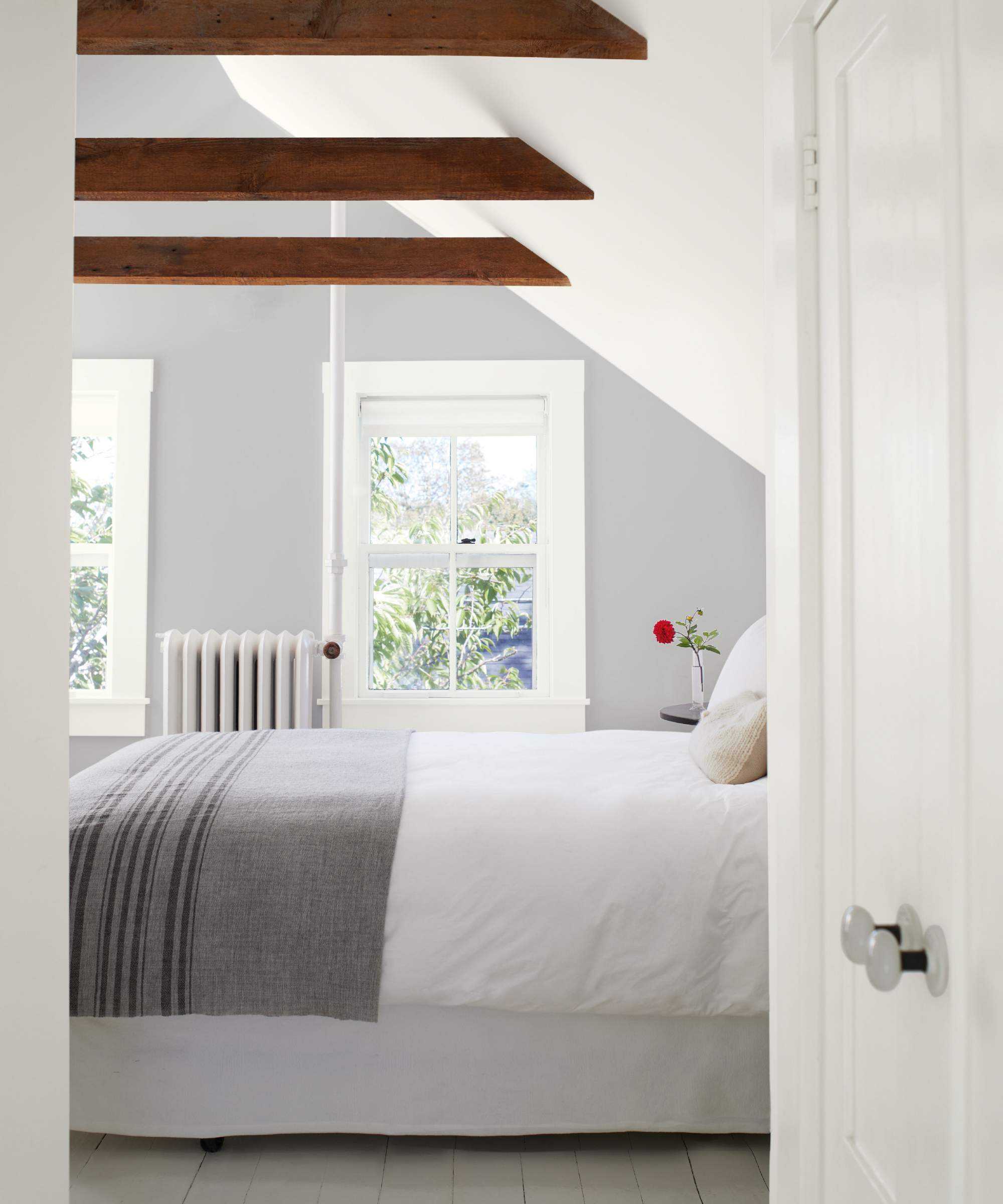 colors that go with light grey, bedroom with light grey and white walls, grey blanket, beams, sloping ceiling, white floor bards, view of garden